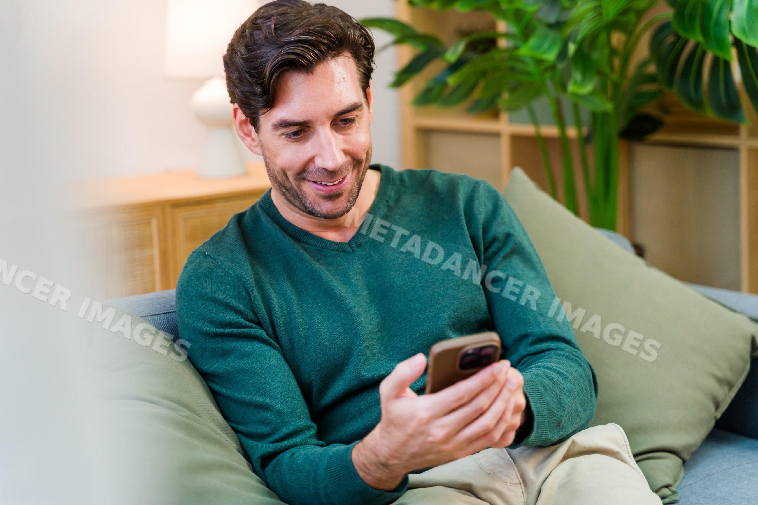 White man holding smartphone sitting on couch in living room