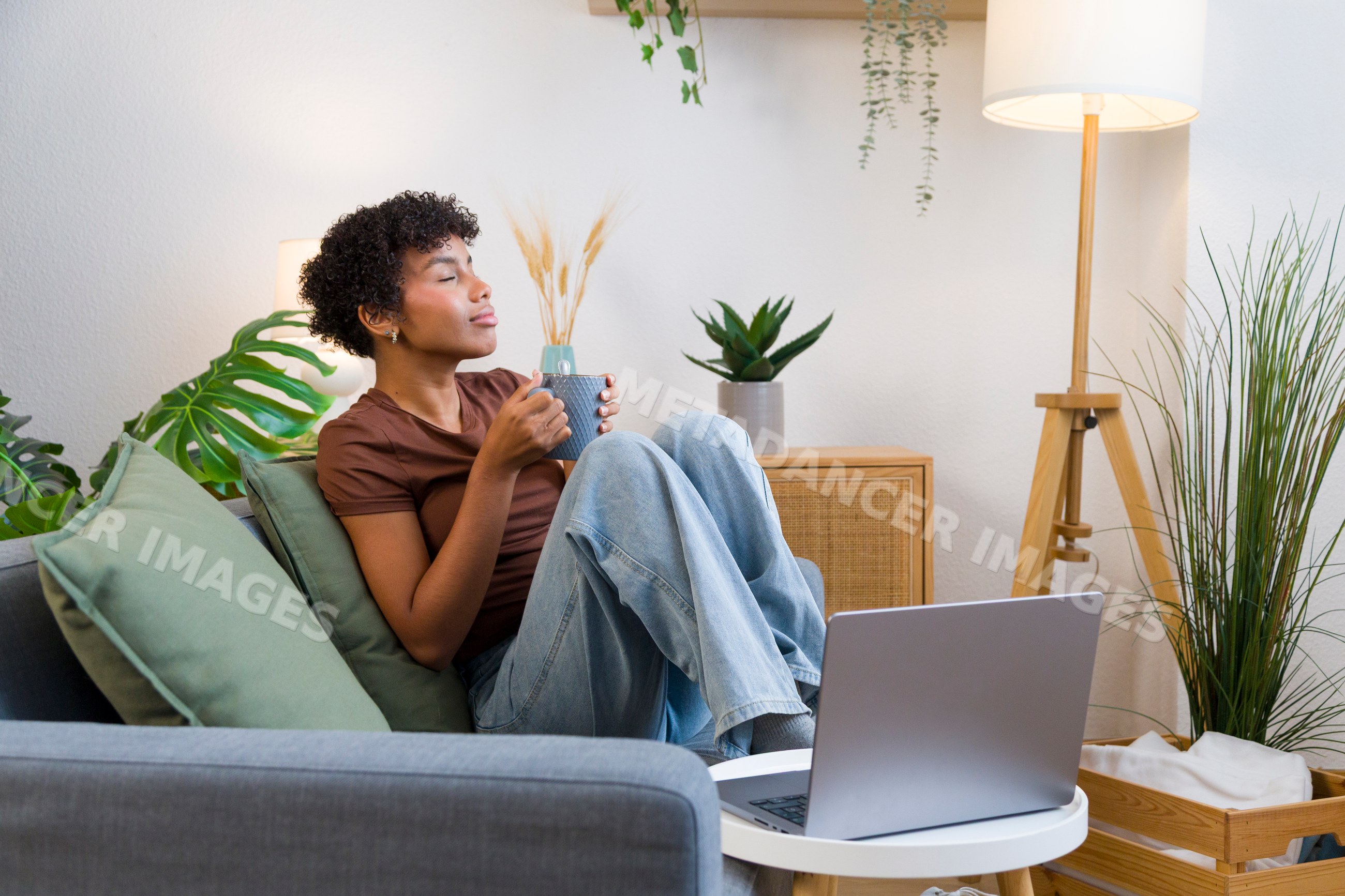 African American woman drinking coffee on sofa with laptop