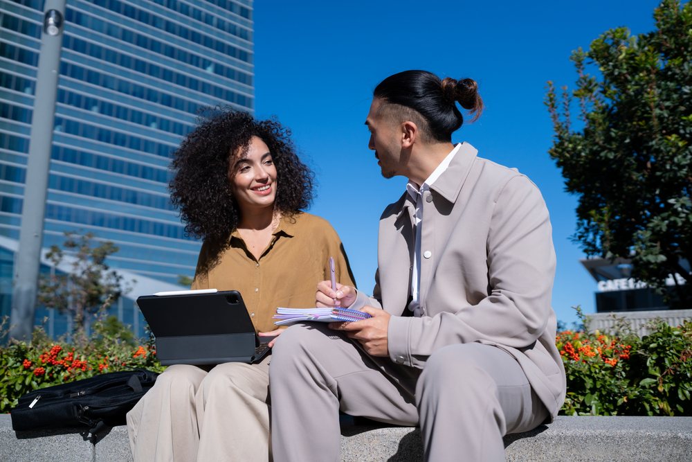 Colleagues discussing work outdoors in Madrid with laptop and notes