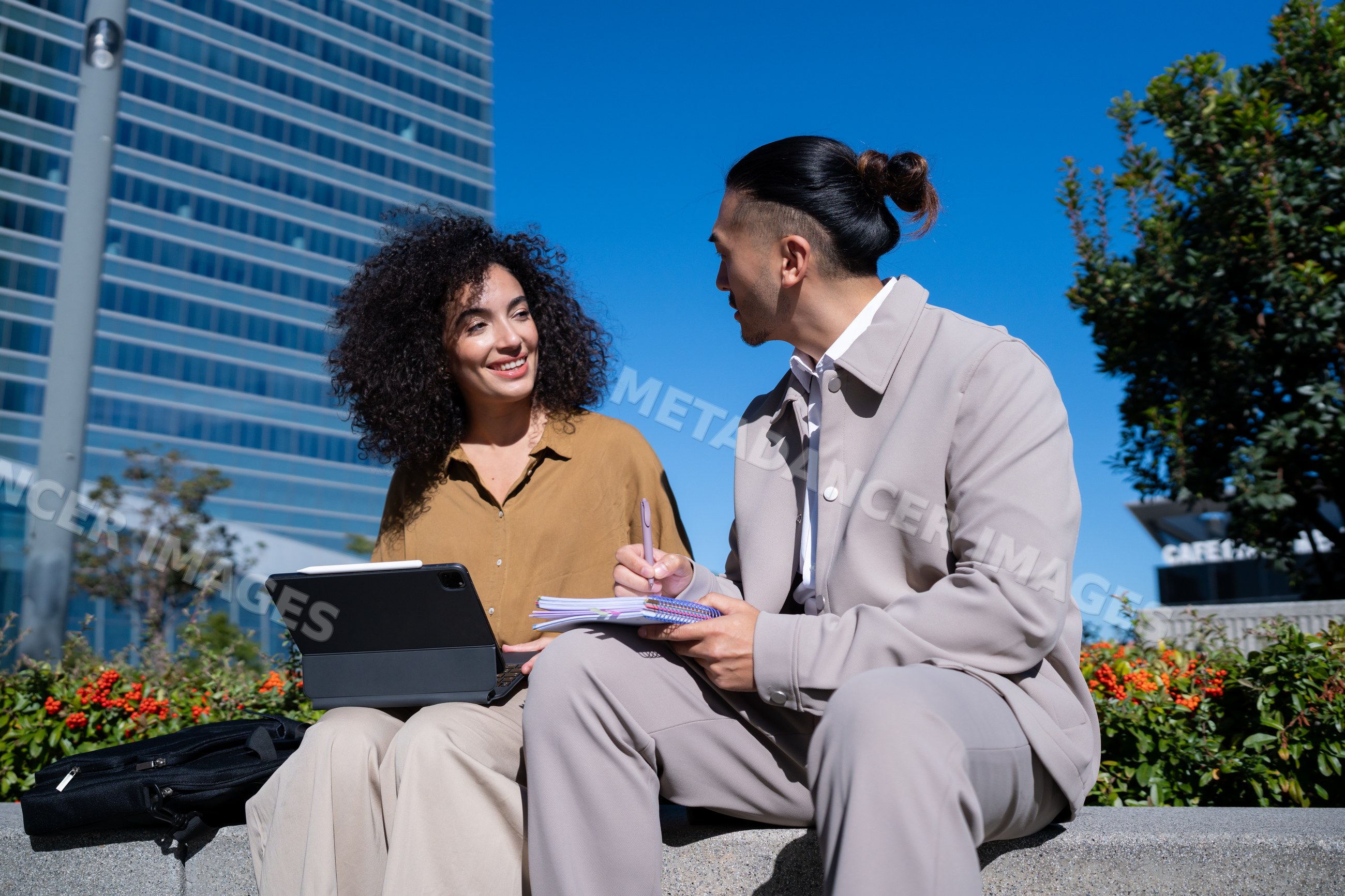 Colleagues discussing work outdoors in Madrid with laptop and notes
