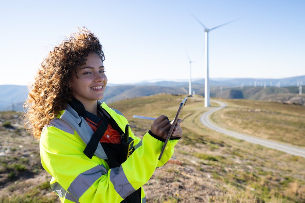 White woman using tablet at wind farm with wind turbines in Galicia
