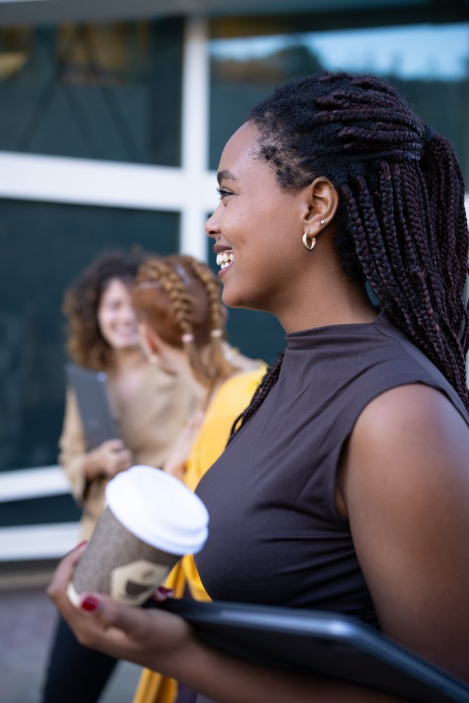 African American and white woman holding coffee cup and laptop