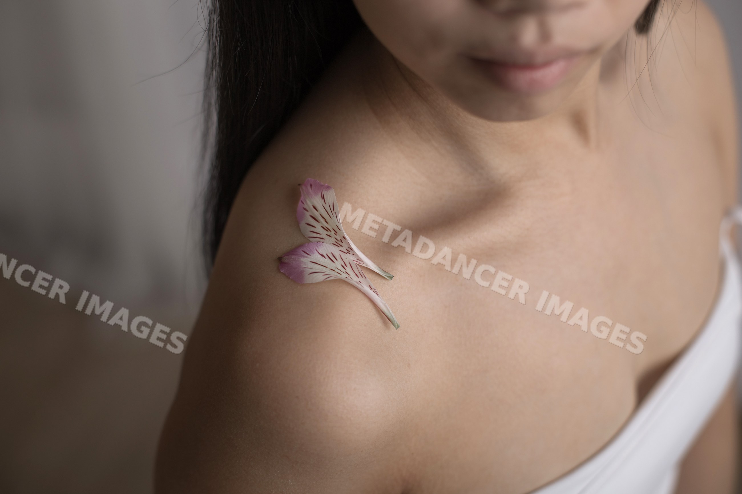 Southeast Asian woman's shoulder with pink flower petals close-up