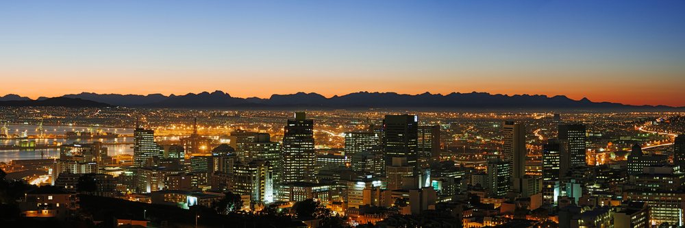 Cityscape at sunset with illuminated buildings and mountains
