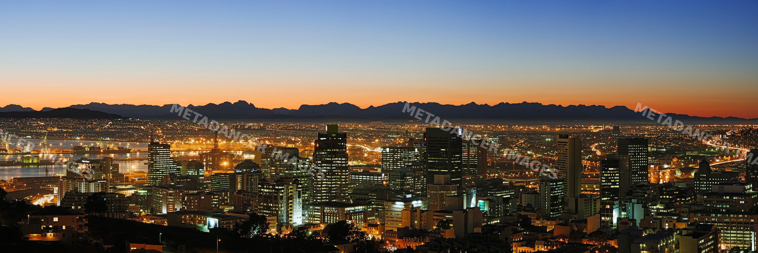 Cityscape at sunset with illuminated buildings and mountains