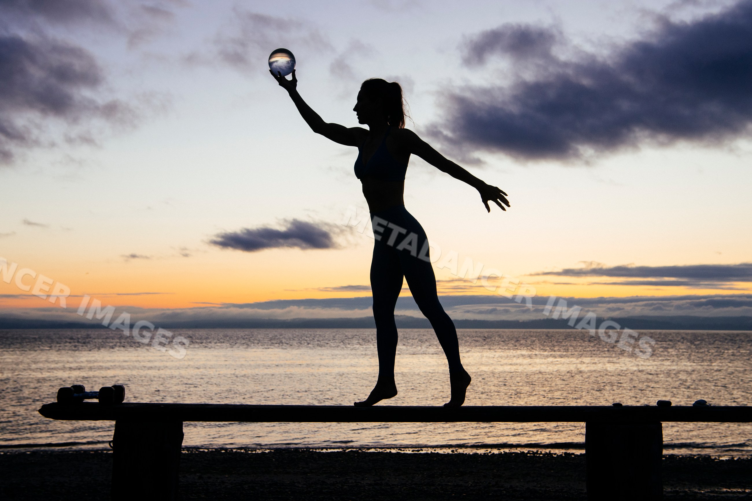 Silhouette of white woman balancing on beam by ocean at sunset