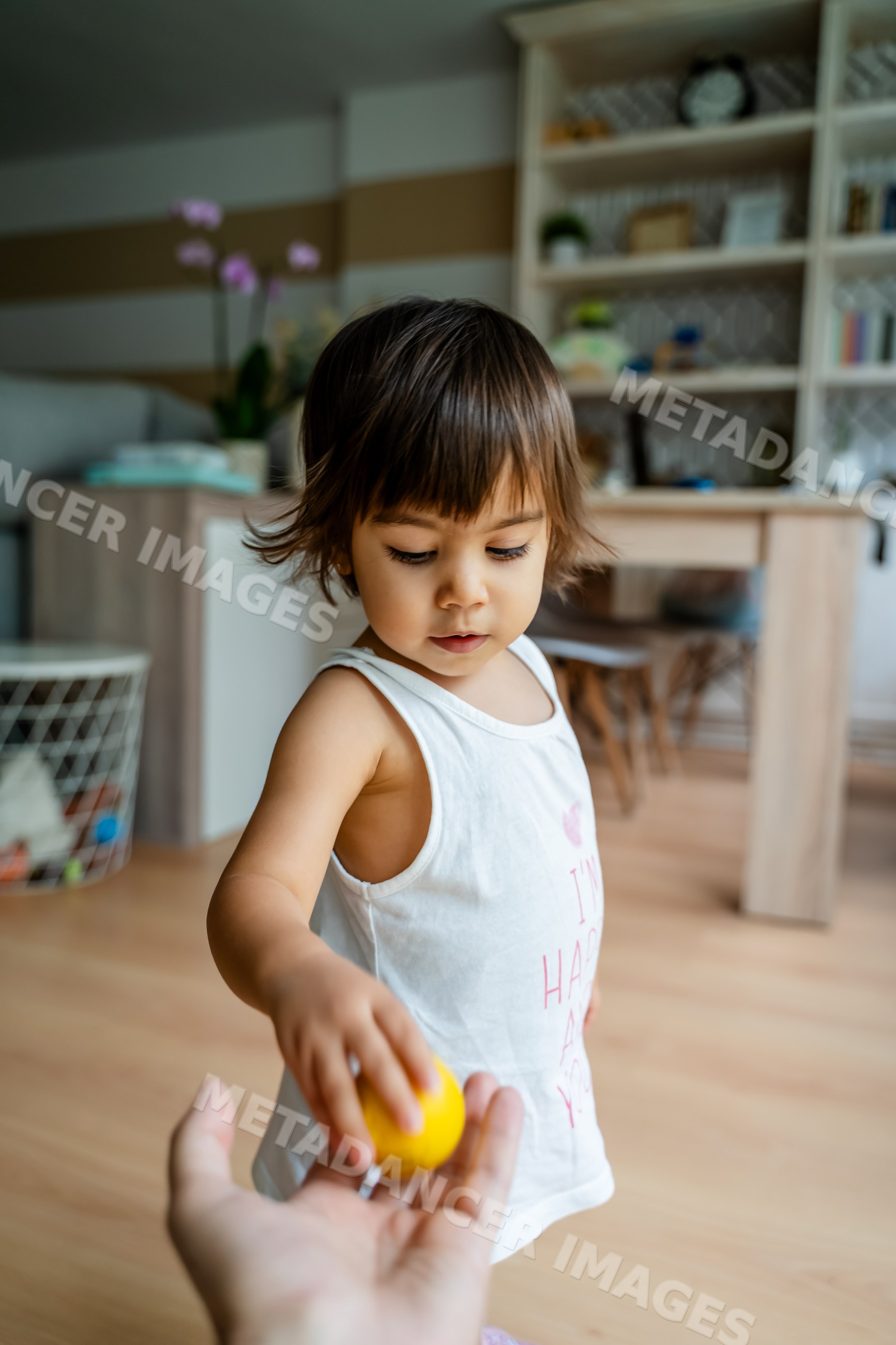 Toddler giving yellow toy ball to white adult hand indoors
