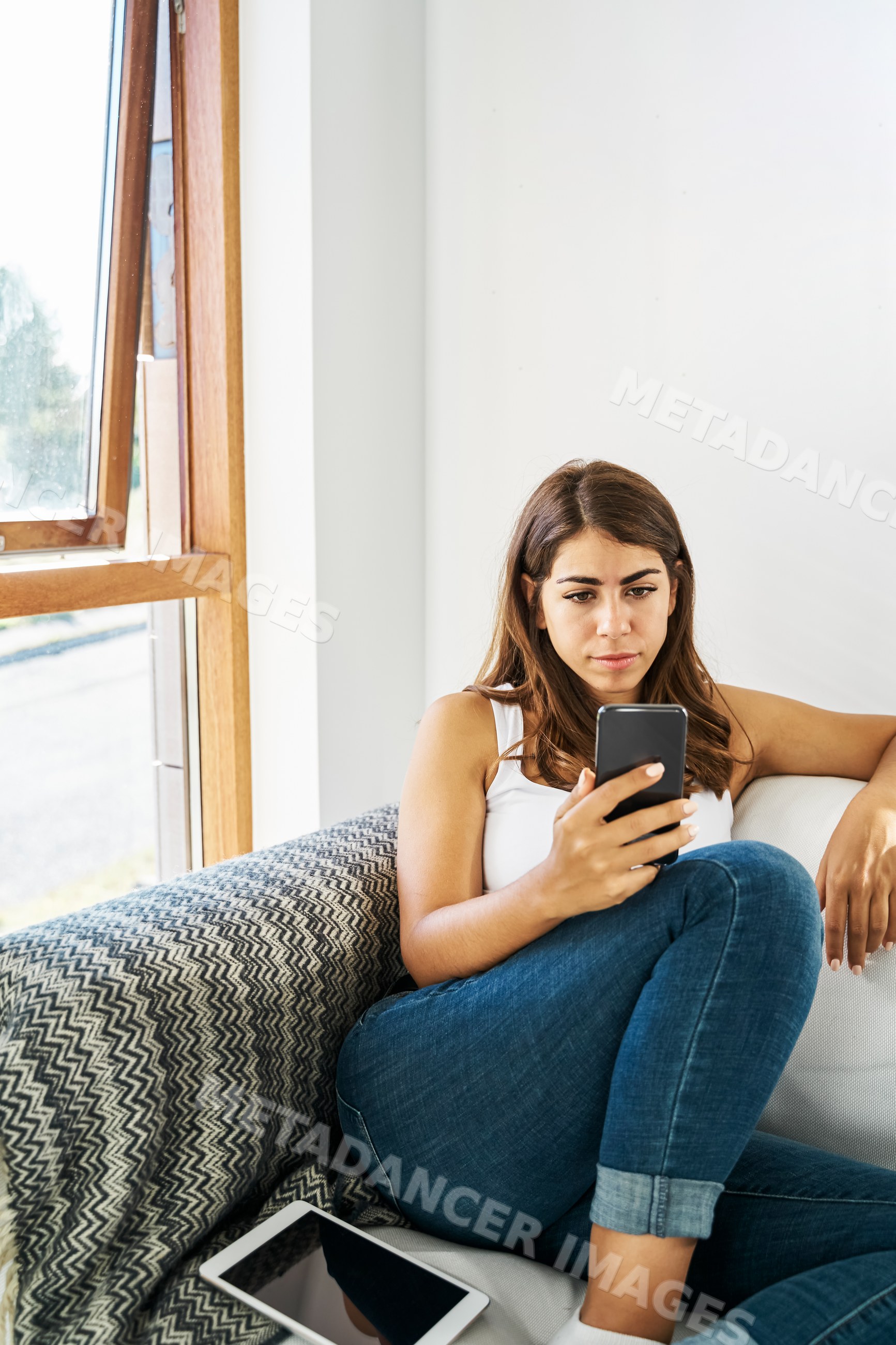 A white woman sits on a couch looking at her phone indoors