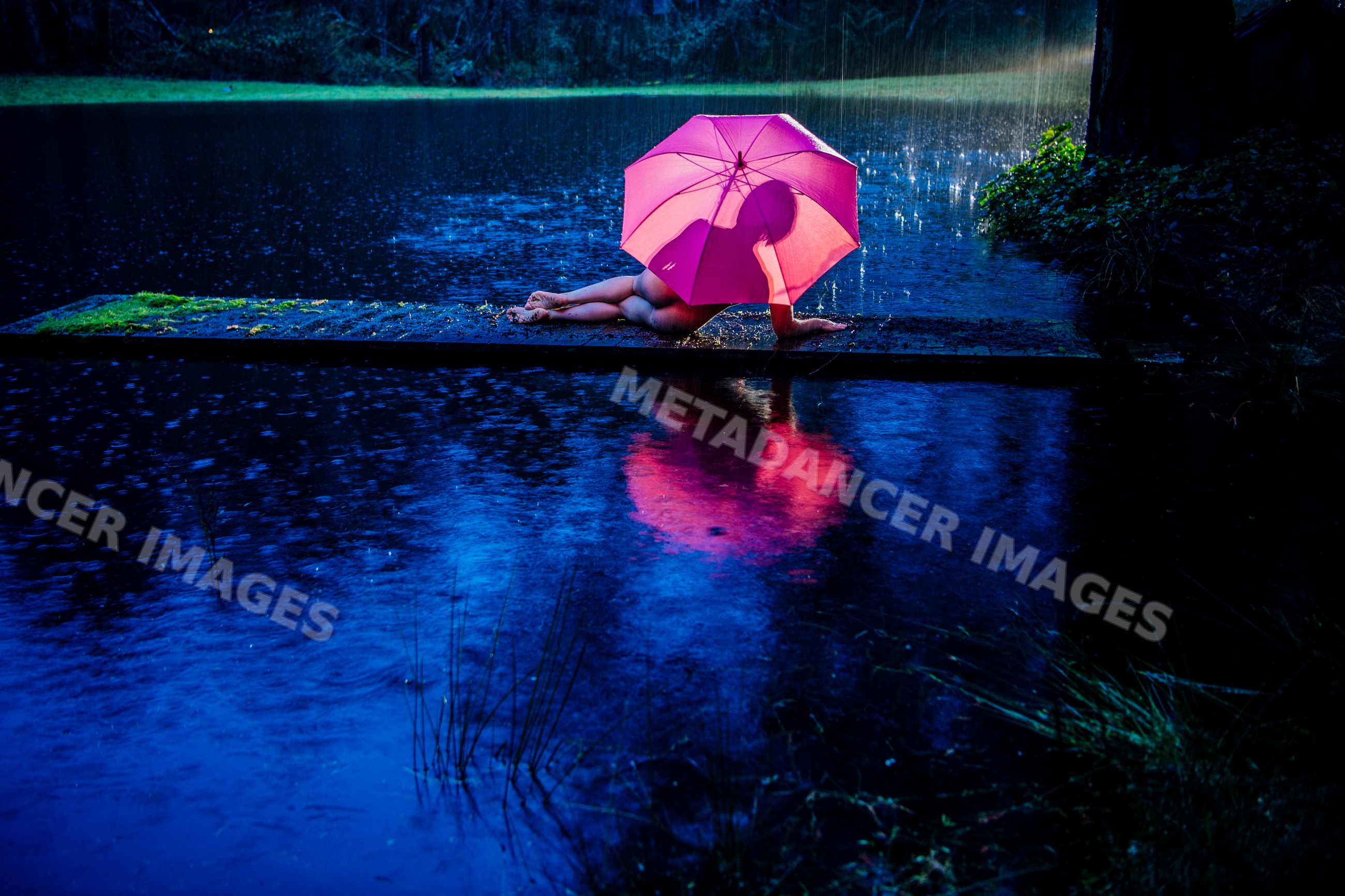 White person lying on pathway with pink umbrella in rainy night