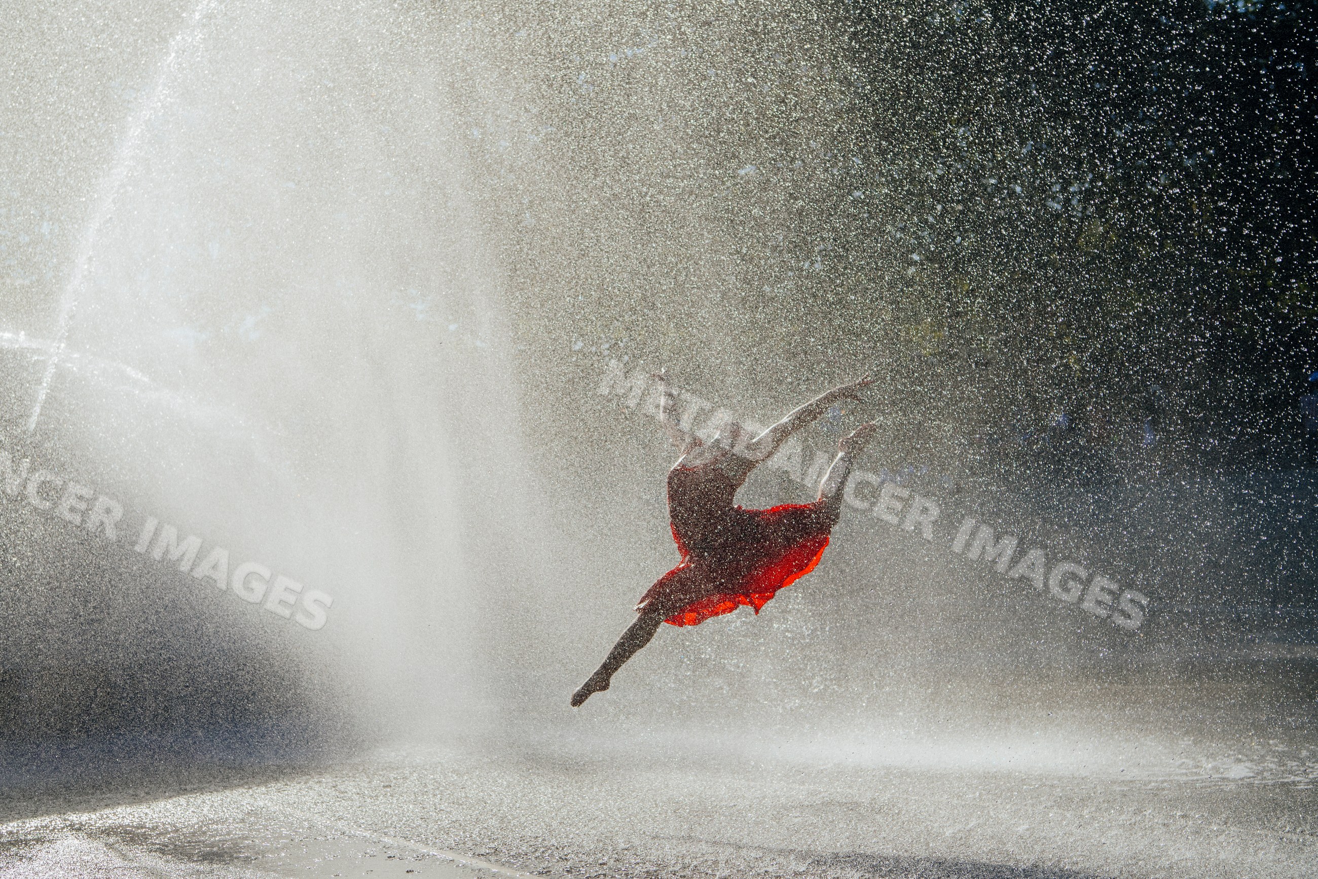 White dancer leaping through fountain spray in red dress outdoors