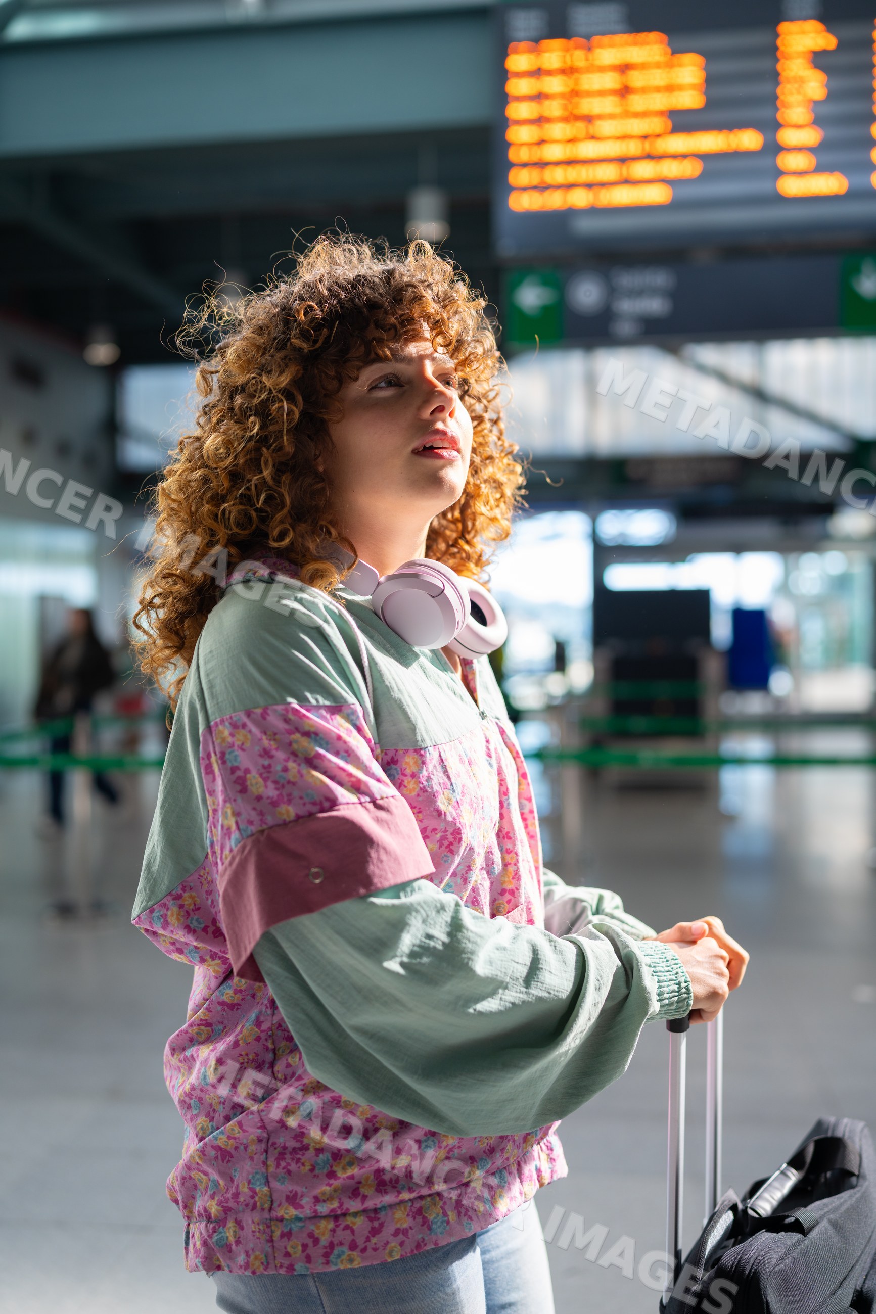 Young white woman waiting in train station with luggage and headphones