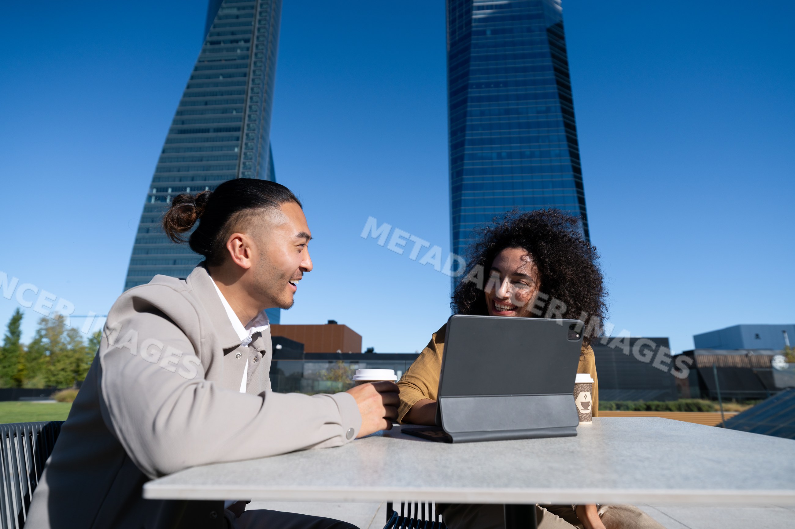 Two people chatting with tablet and coffee at outdoor city cafe