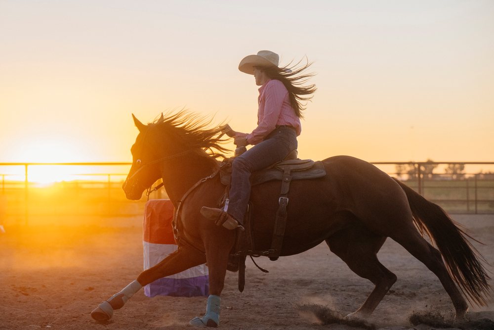 White woman riding horse at sunset in outdoor arena