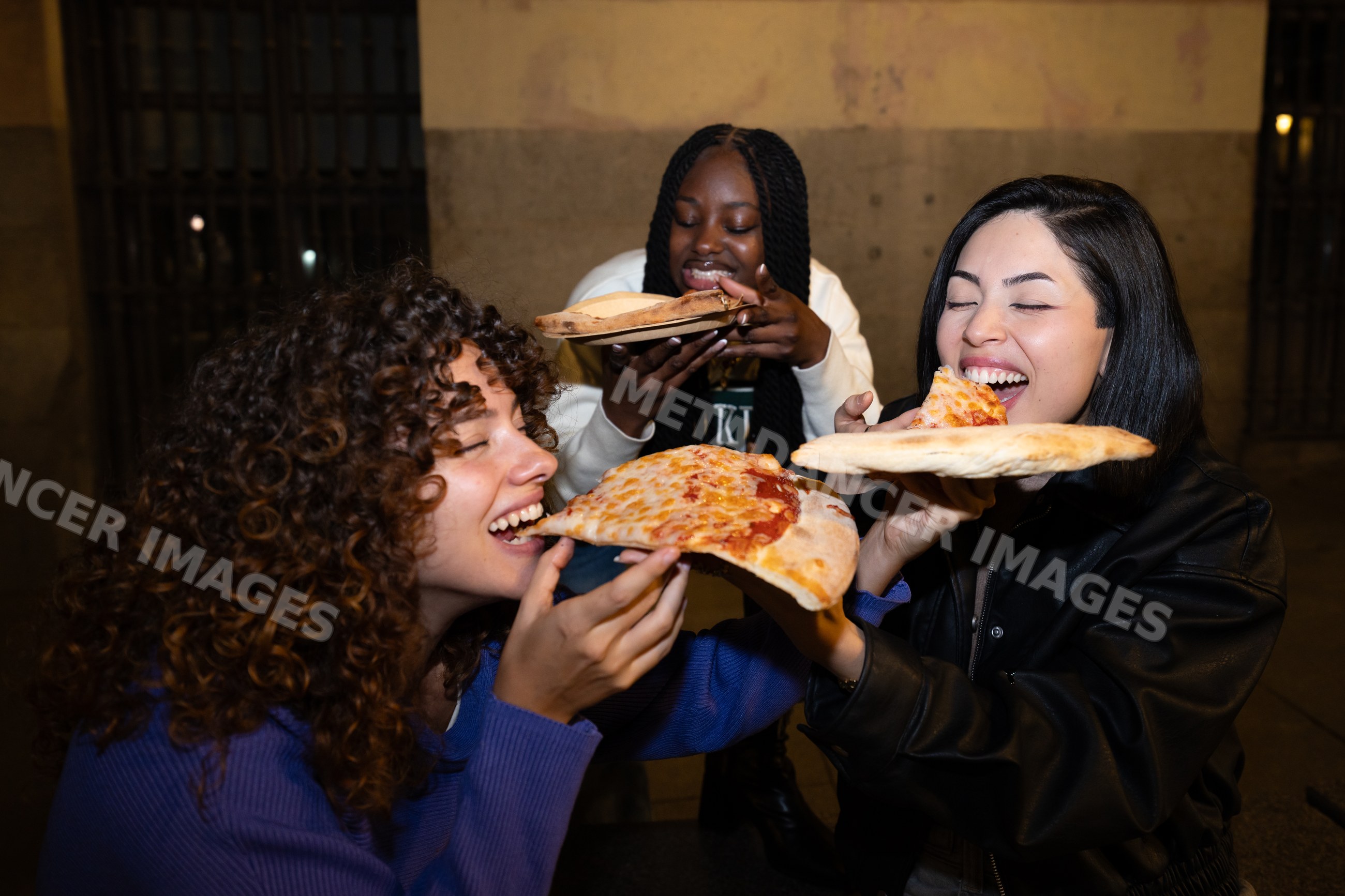 Three Hispanic, white and Black women eating cheese pizza outdoors