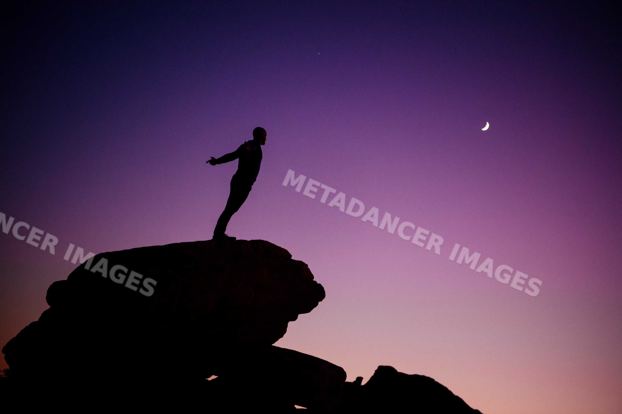 Silhouette of white man standing on rock under crescent moon