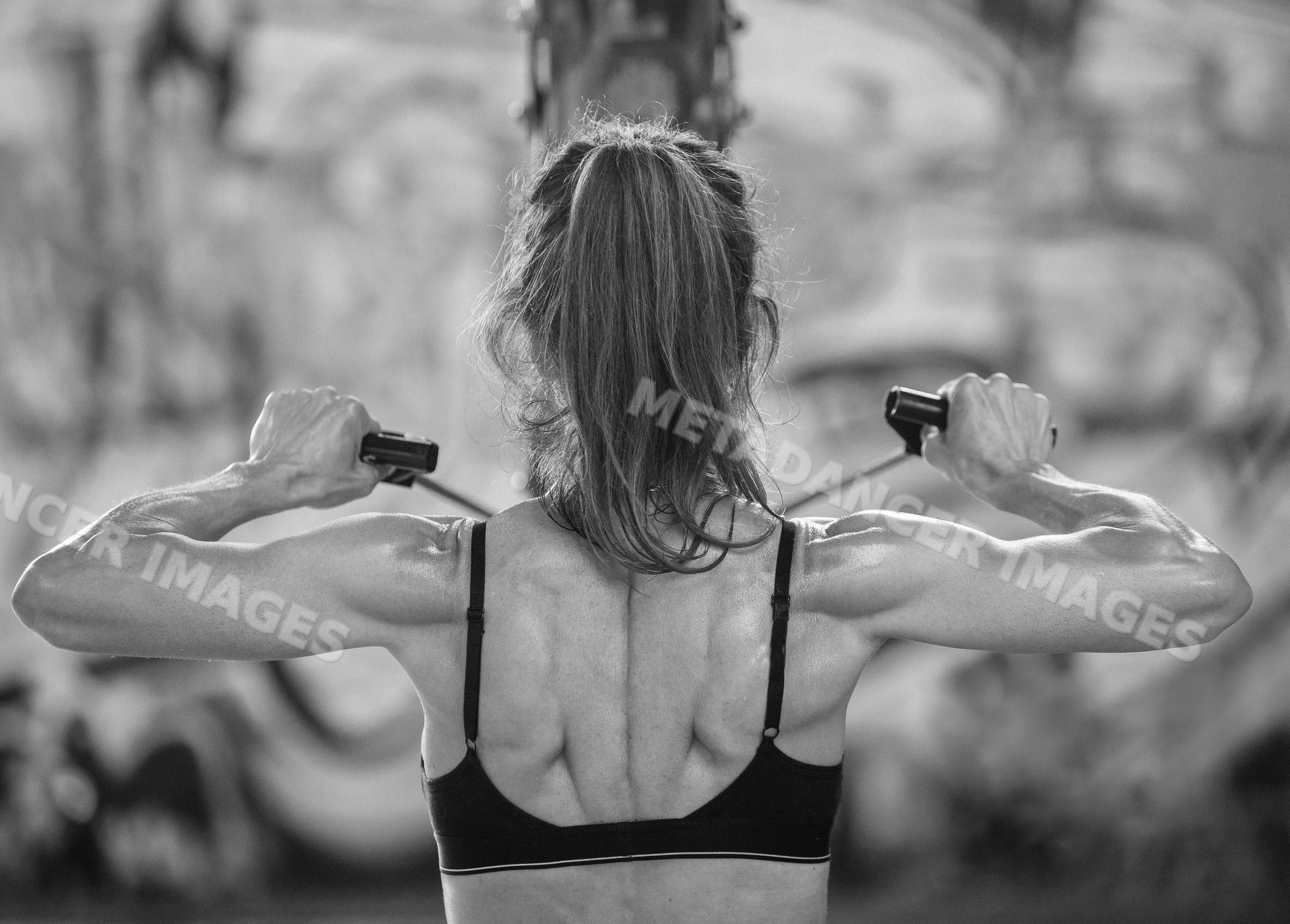 White woman building back muscles with cable machine workout in gym