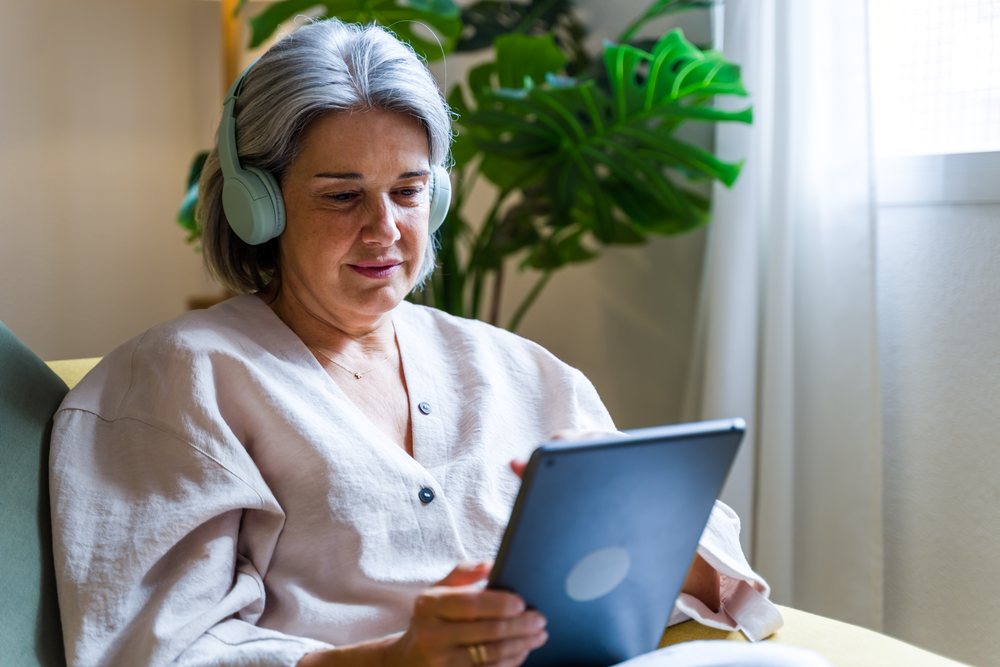White woman wearing headphones using tablet indoors near houseplant