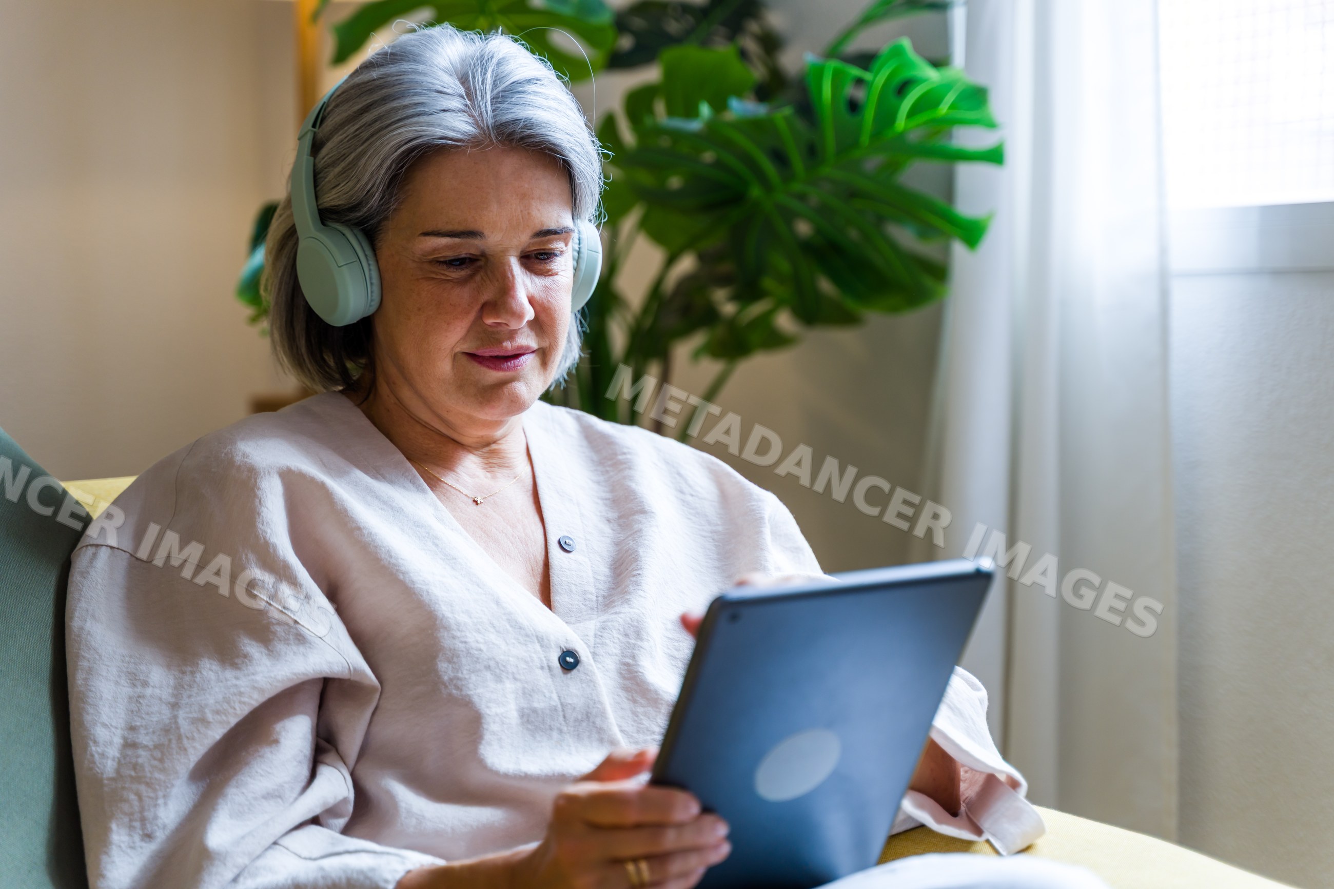White woman wearing headphones using tablet indoors near houseplant
