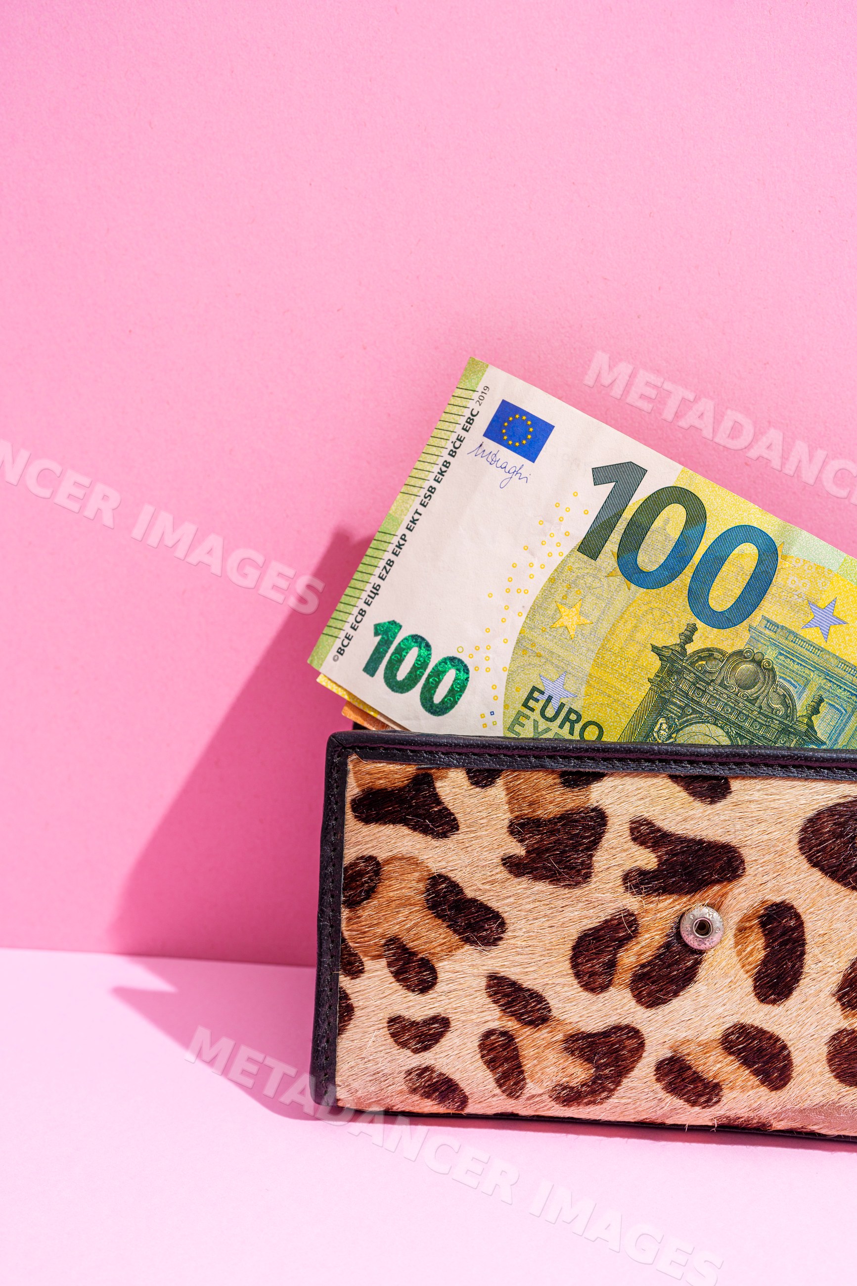 Leopard print wallet with 100 euro banknotes on pink studio background