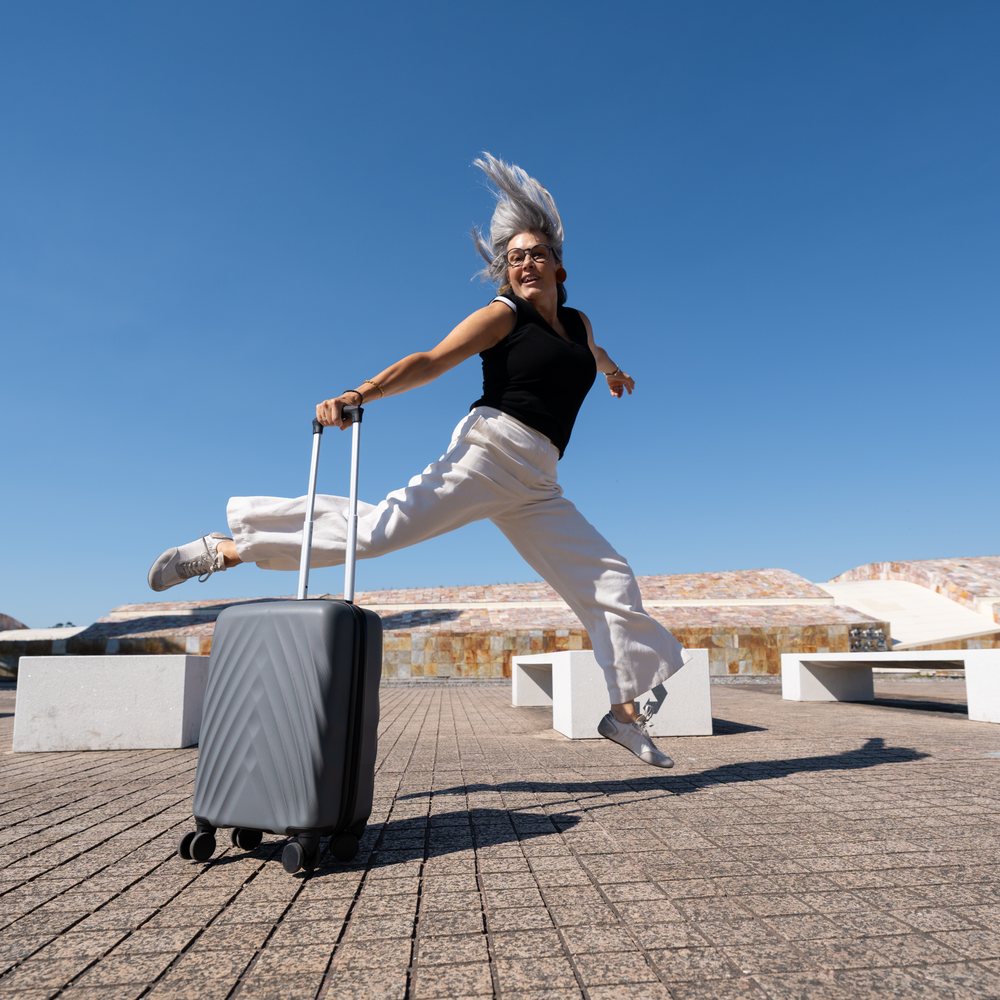 White woman jumping with suitcase in bright urban outdoor setting