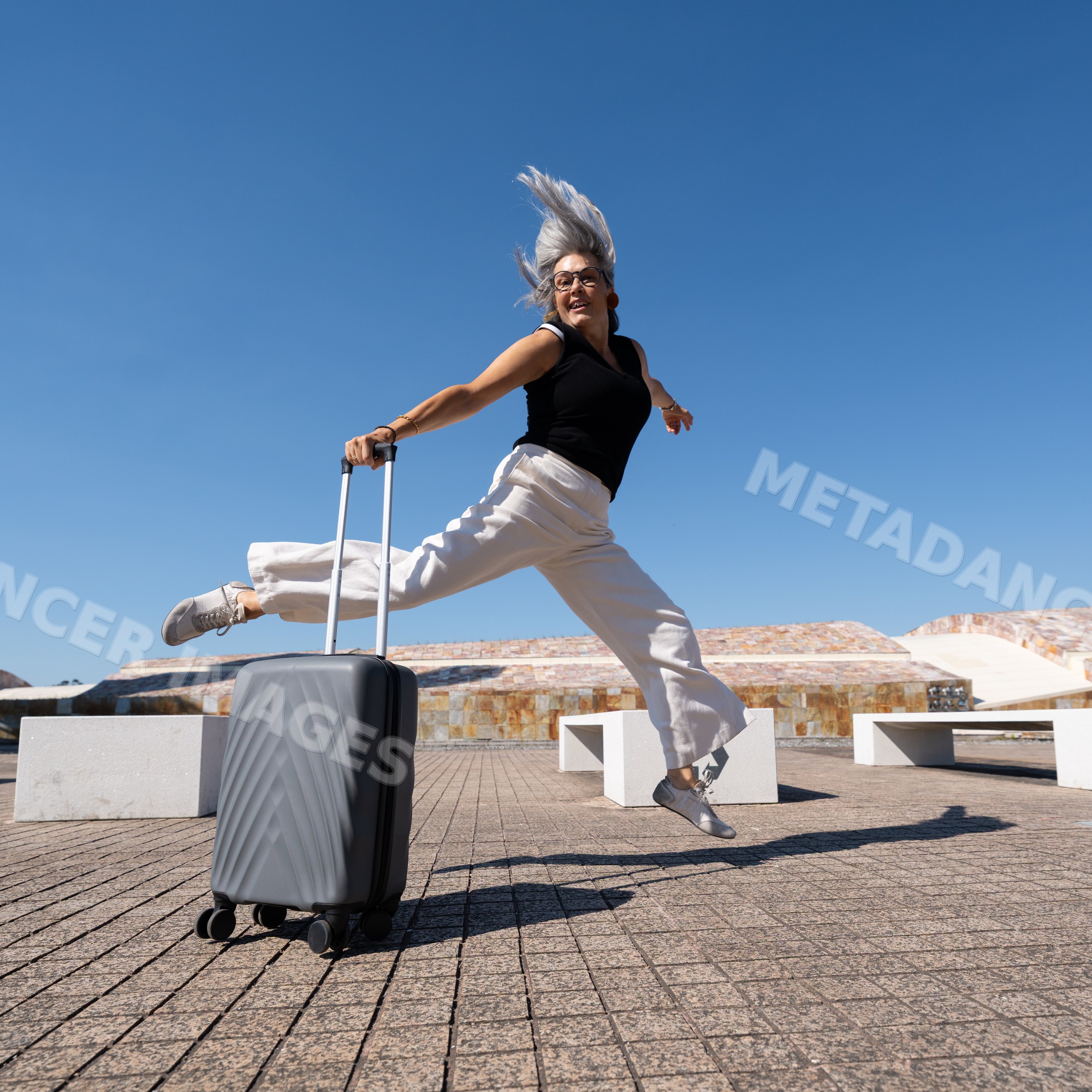White woman jumping with suitcase in bright urban outdoor setting