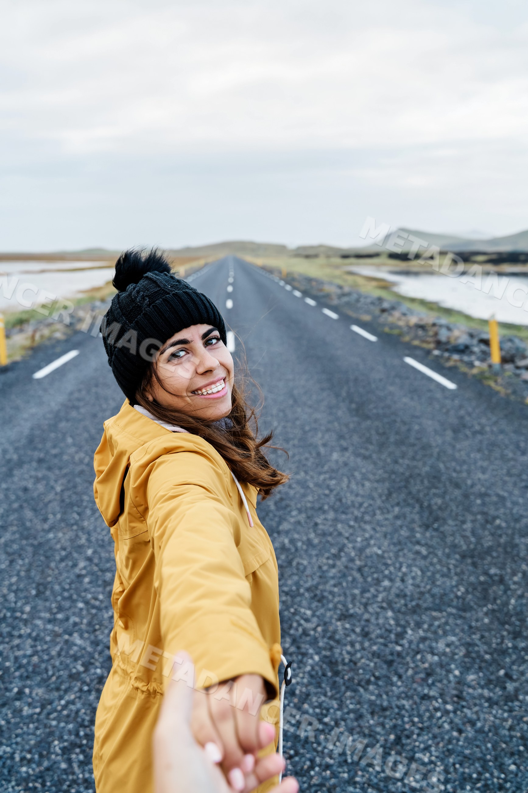 White Woman in warm clothing holding hands and smiling on an open road