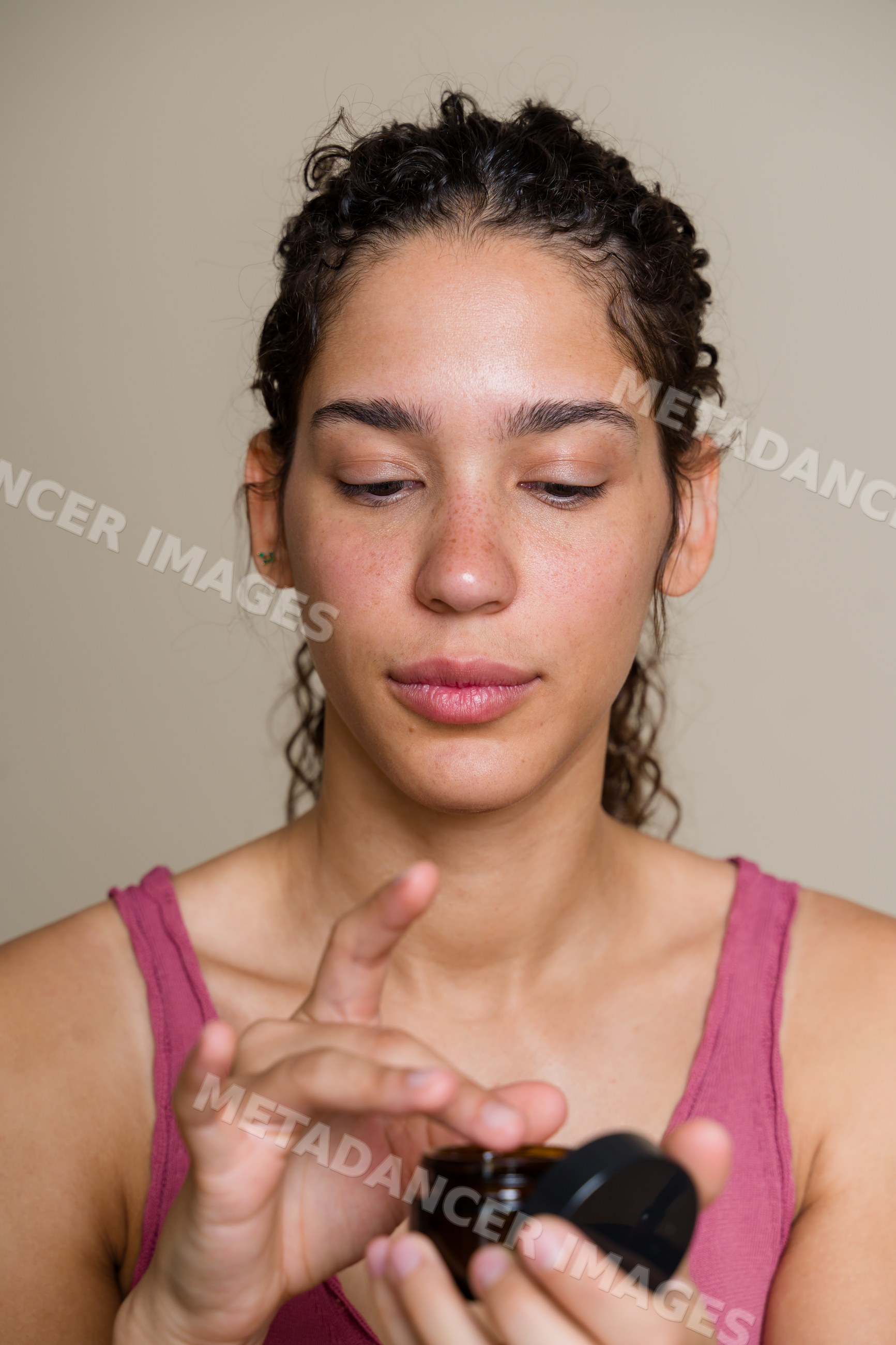 Hispanic woman applying cream from jar in a beauty shoot