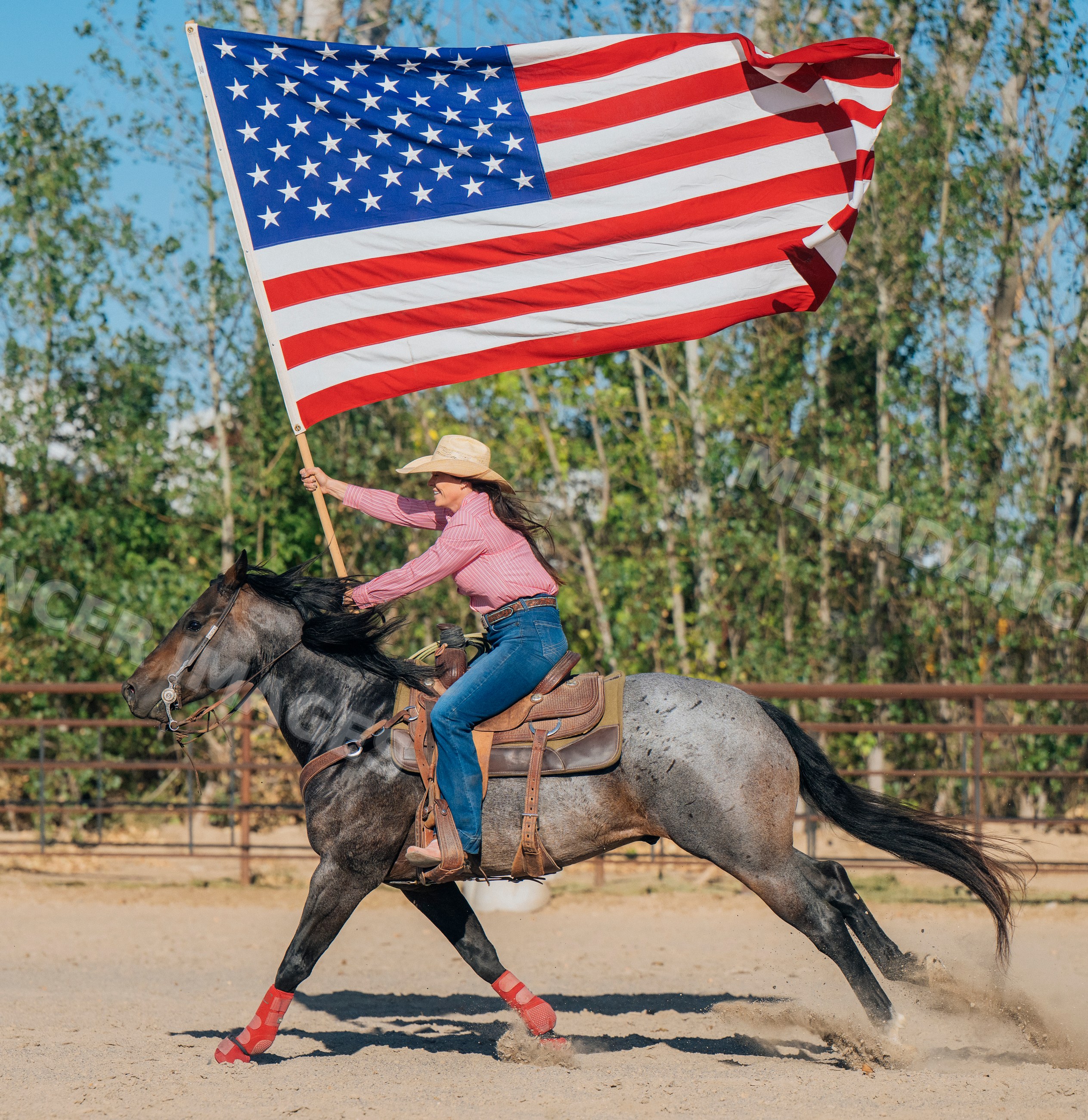 White woman riding horse holding american flag in outdoor arena