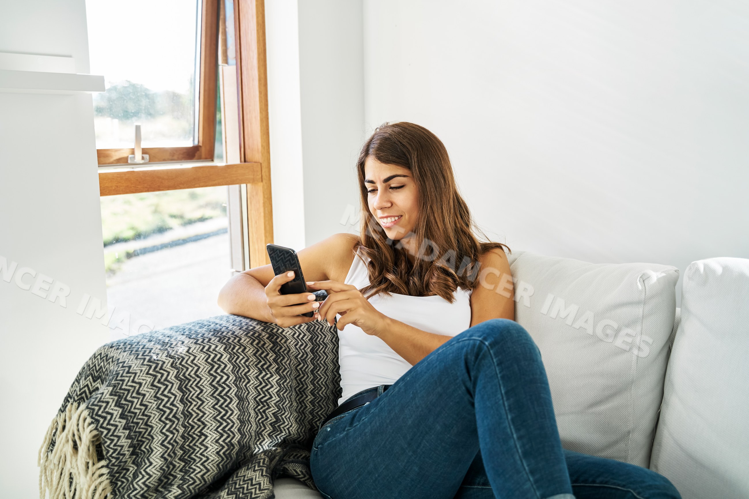 A white woman relaxing on a couch and using her smartphone indoors