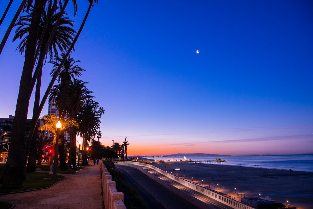 Santa Monica pier and beach at dusk with palm trees and crescent moon