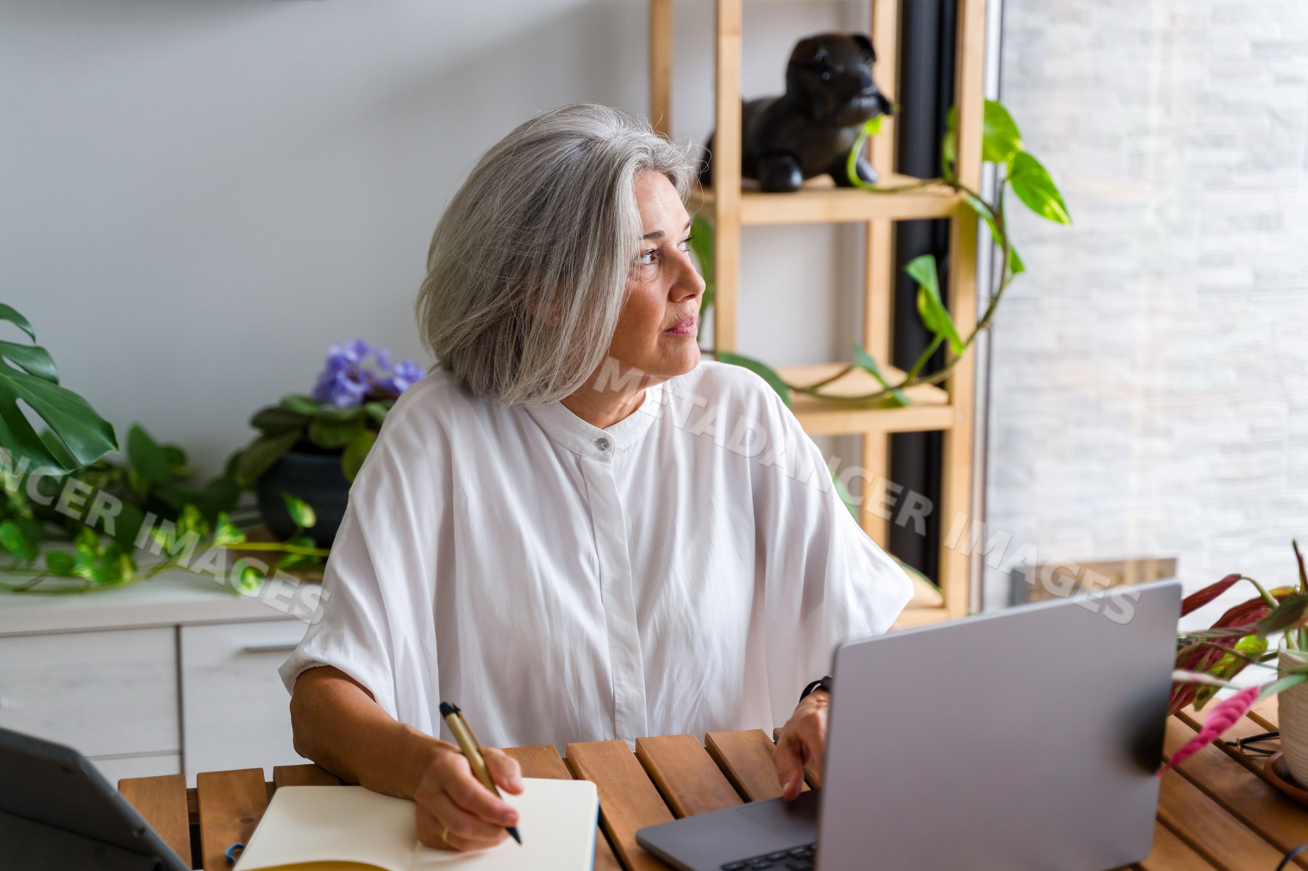 Mature white woman writing notes with laptop in home office in Spain