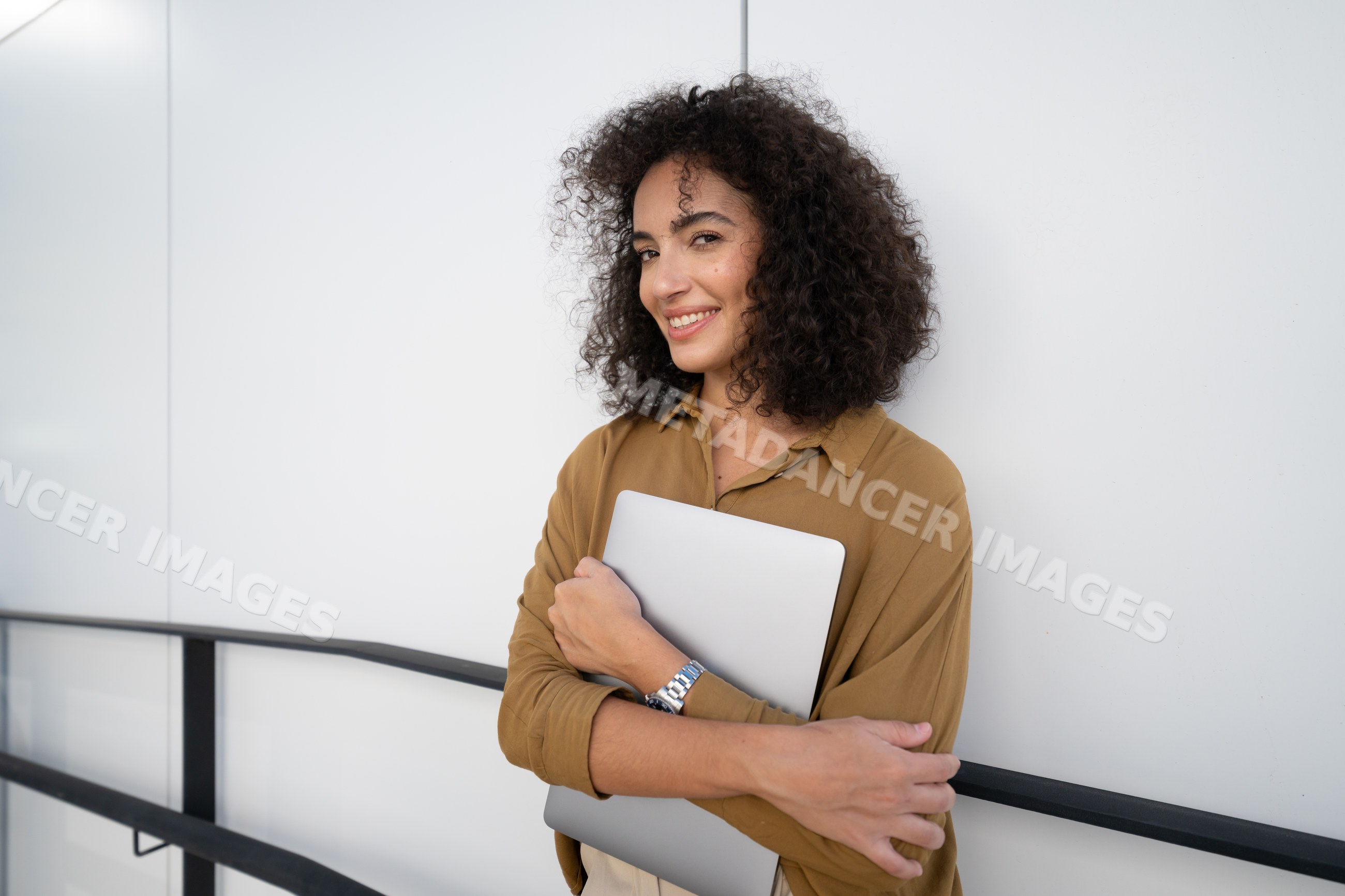 Woman holding laptop and smiling against white wall