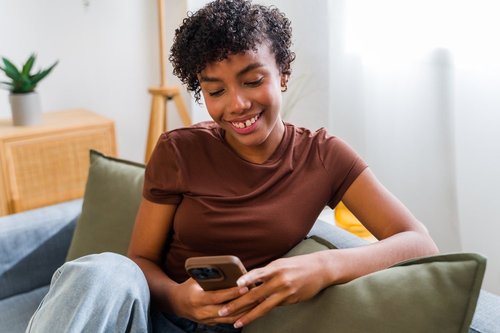 African American woman smiling on couch using smartphone