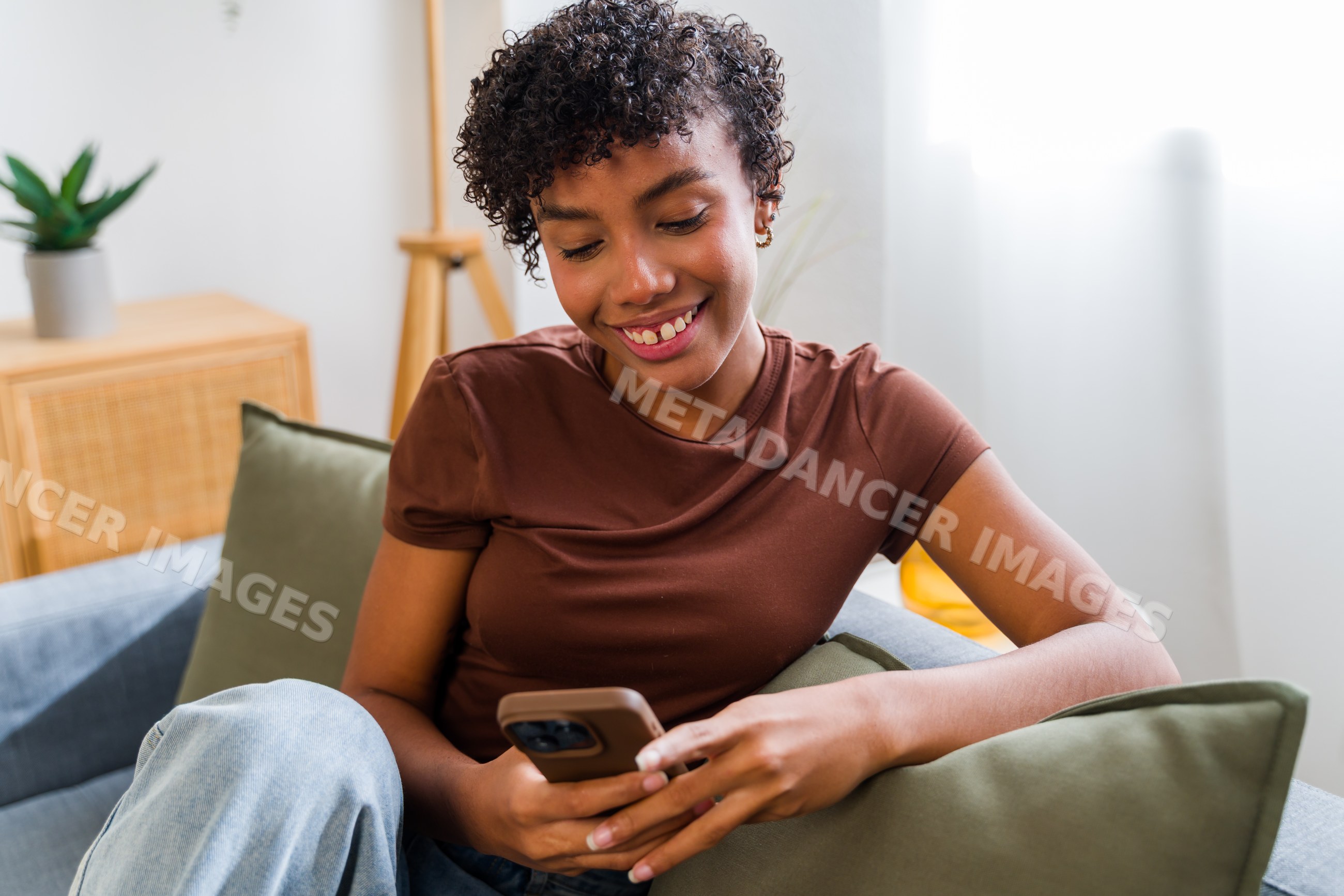 African American woman smiling on couch using smartphone
