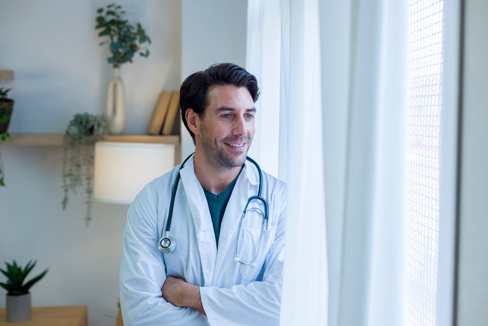 Male doctor looking out window in home office