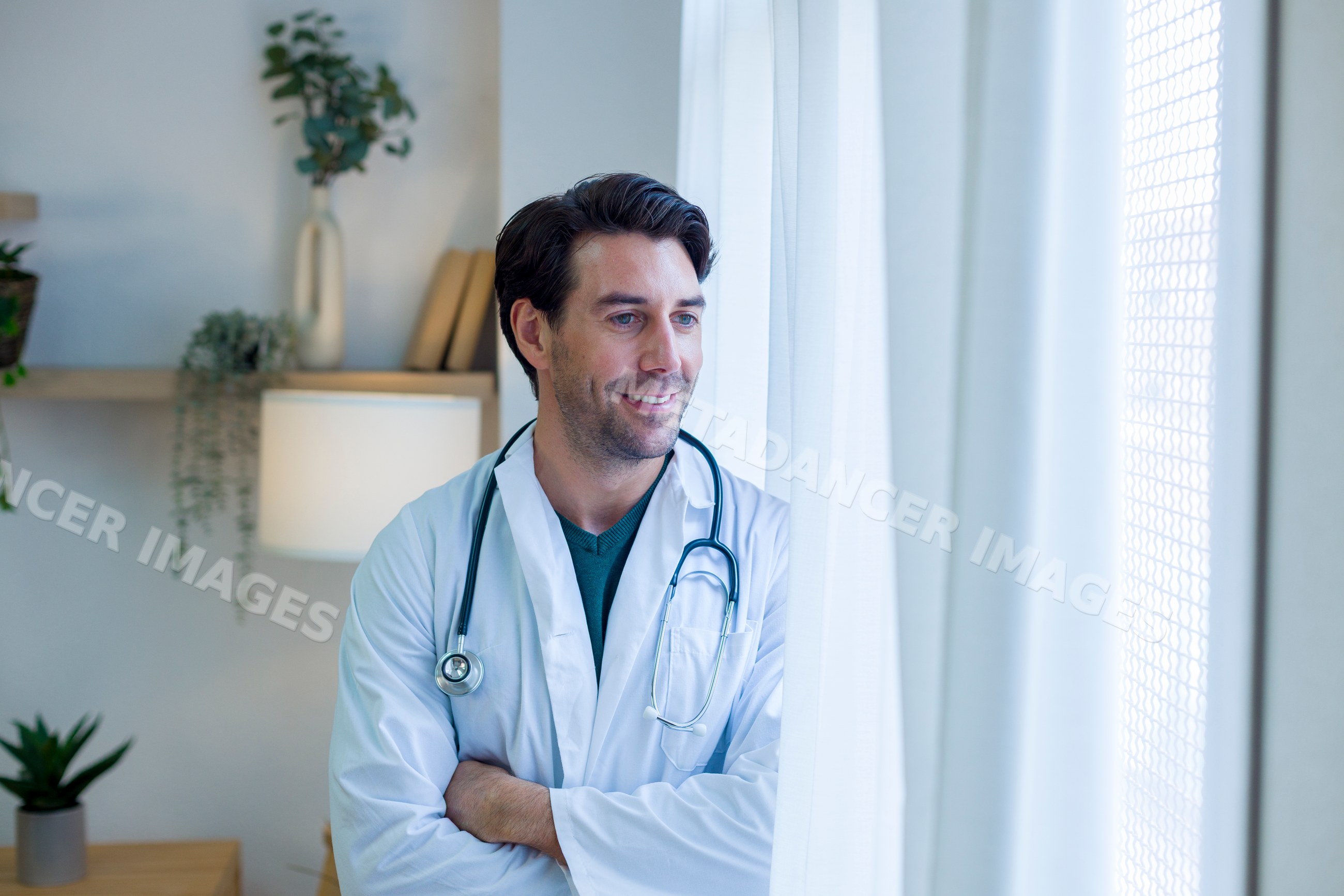 Male doctor looking out window in home office