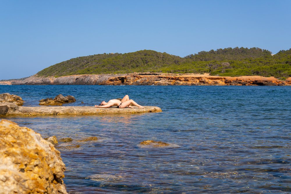 White woman sunbathing on rocky shore by sea in Ibiza, Spain