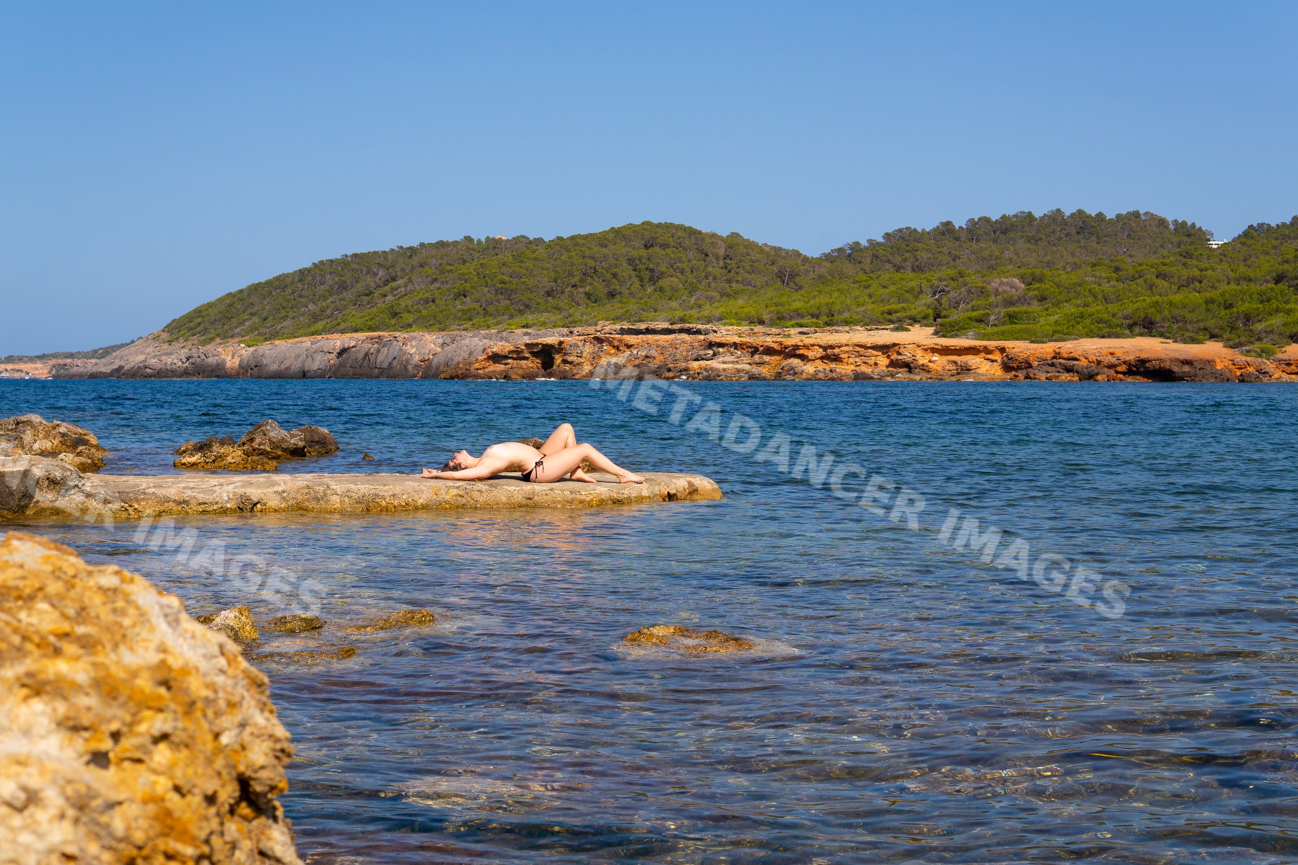White woman sunbathing on rocky shore by sea in Ibiza, Spain