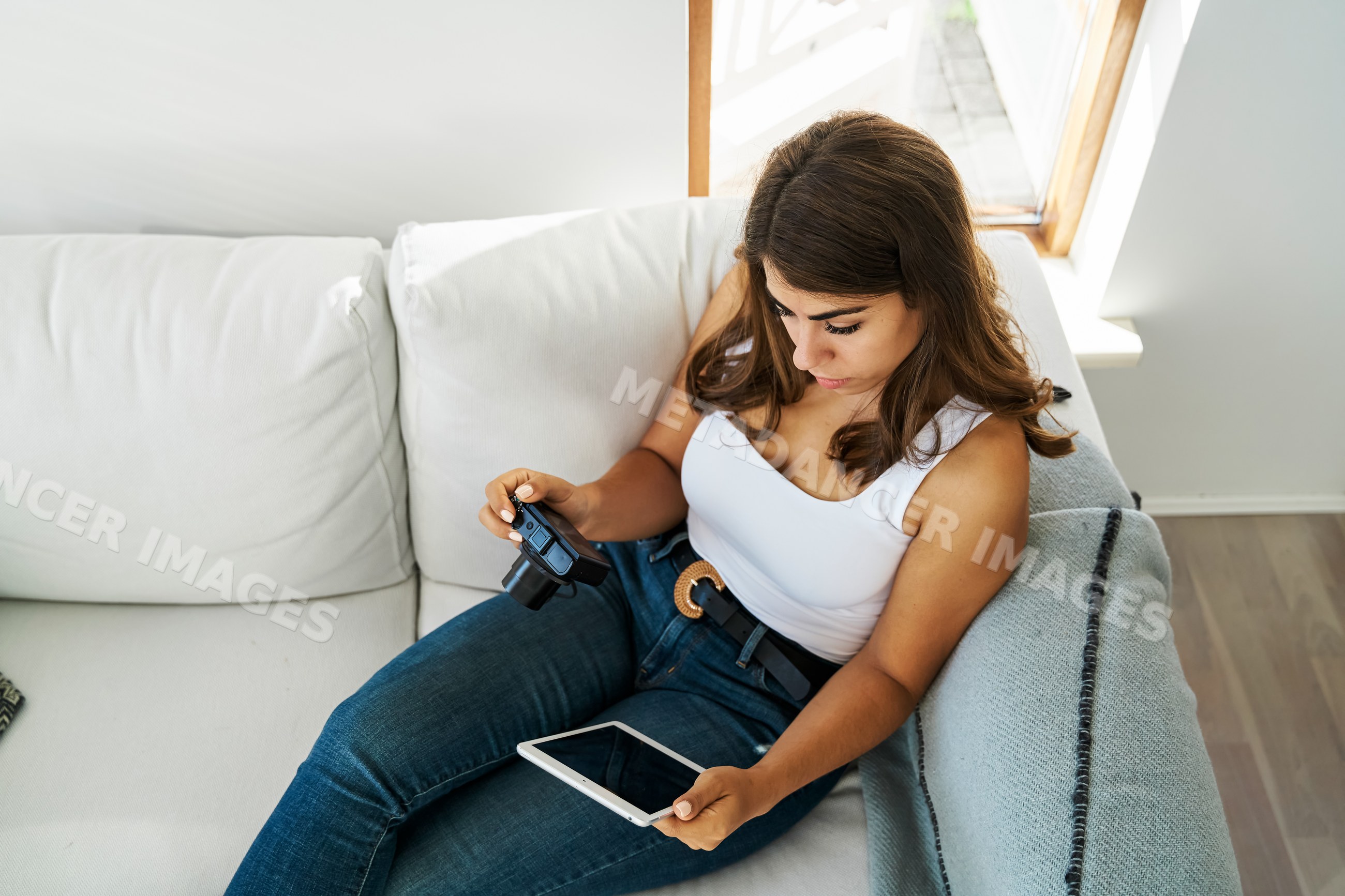 A white woman uses a digital camera and tablet while seated on a sofa