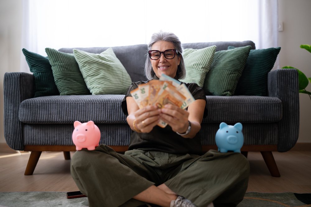 White woman holding money sitting cross-legged on floor with piggy