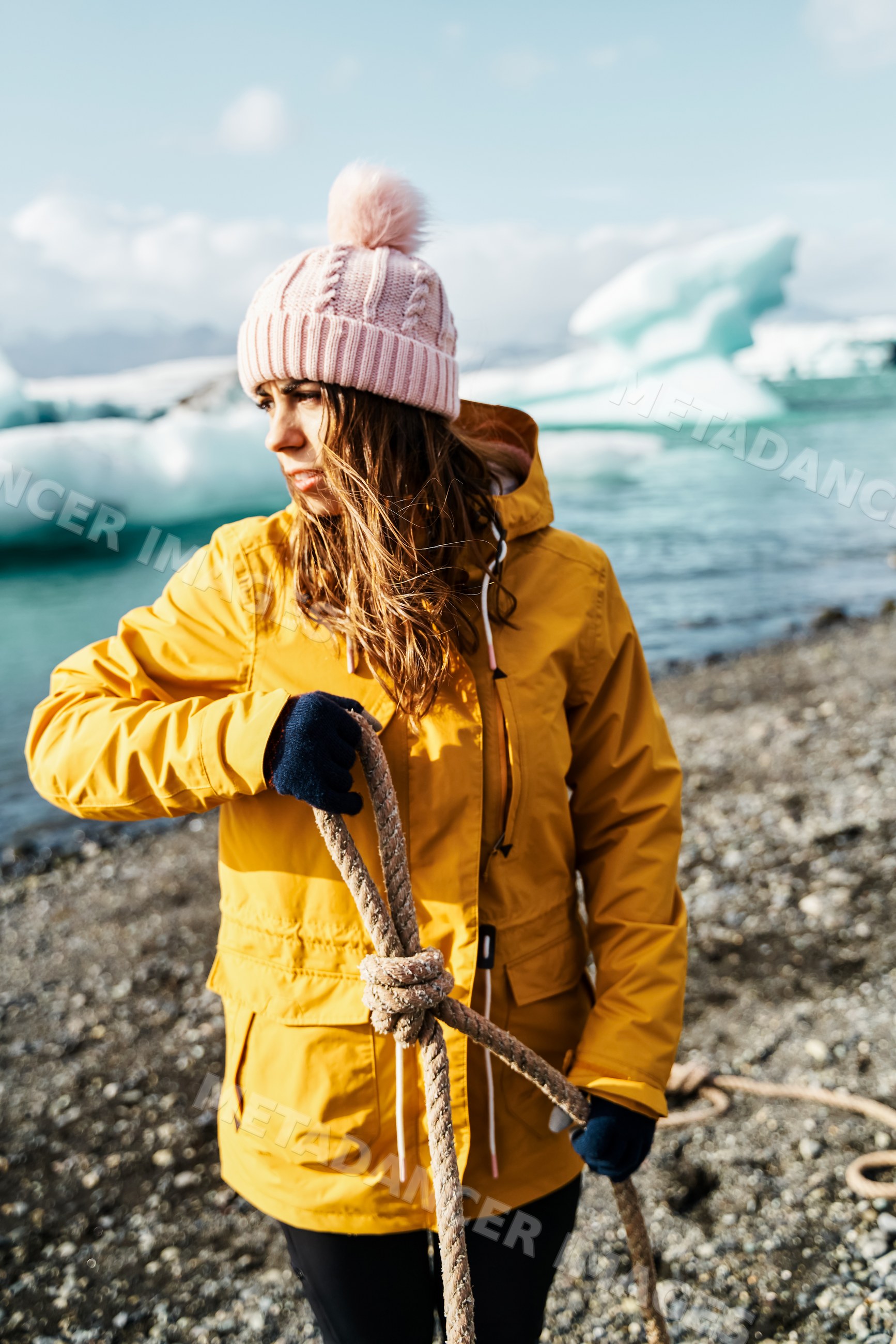 A white woman holding a rope on a rocky shore with icebergs