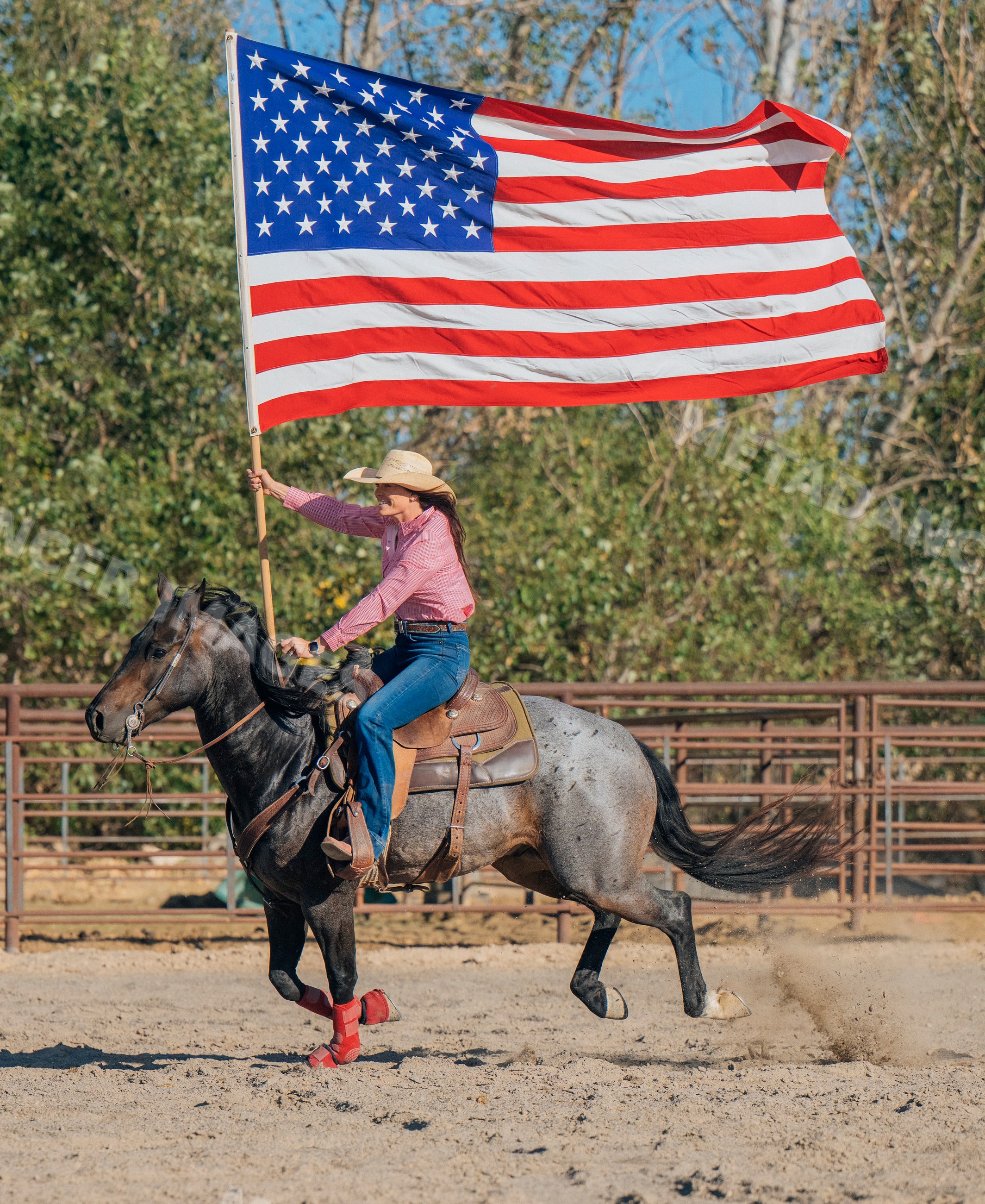 White woman riding horse carrying american flag in rodeo arena