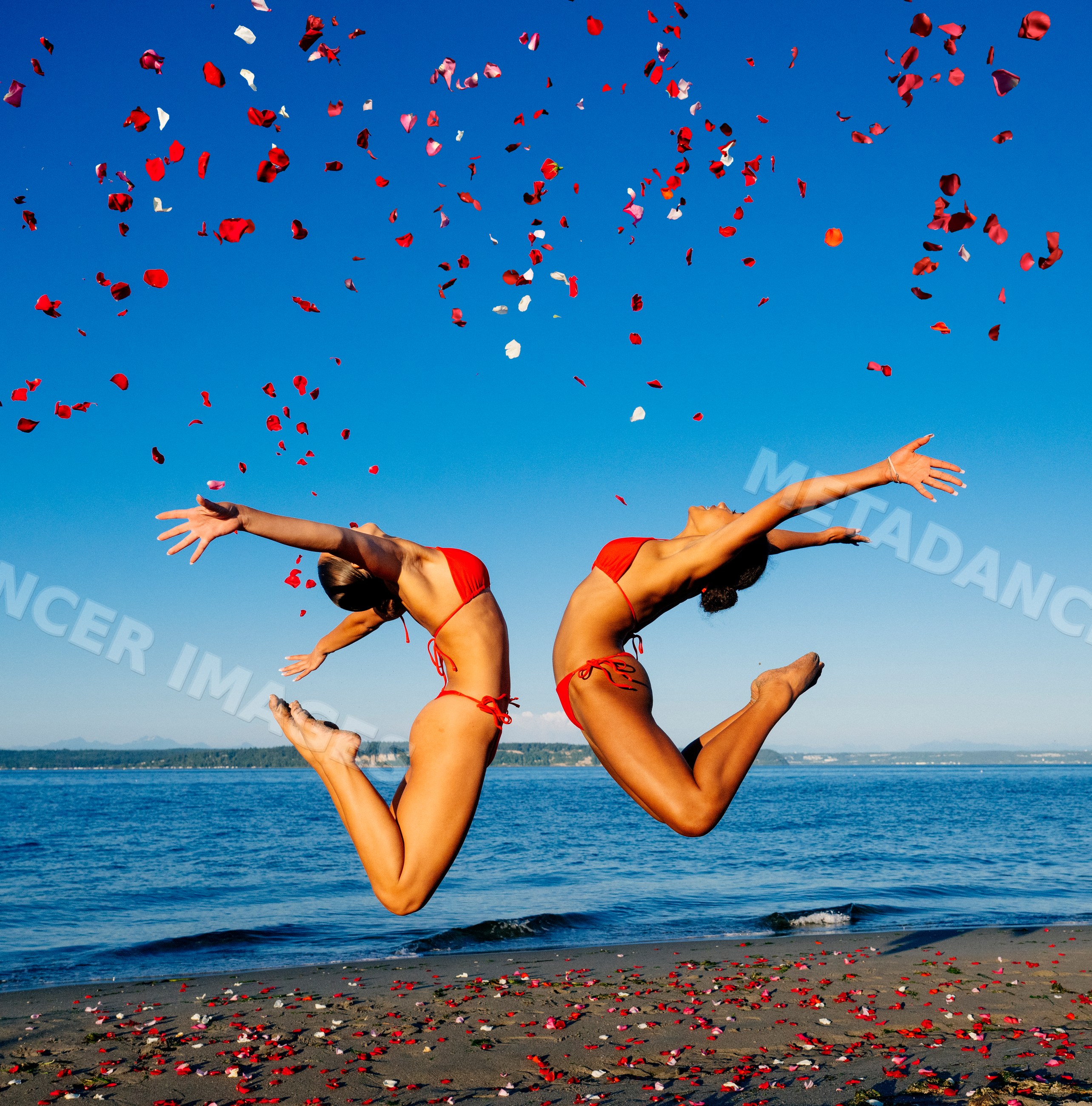 Two women in red swimwear jump on a beach with rose petals in wa USA
