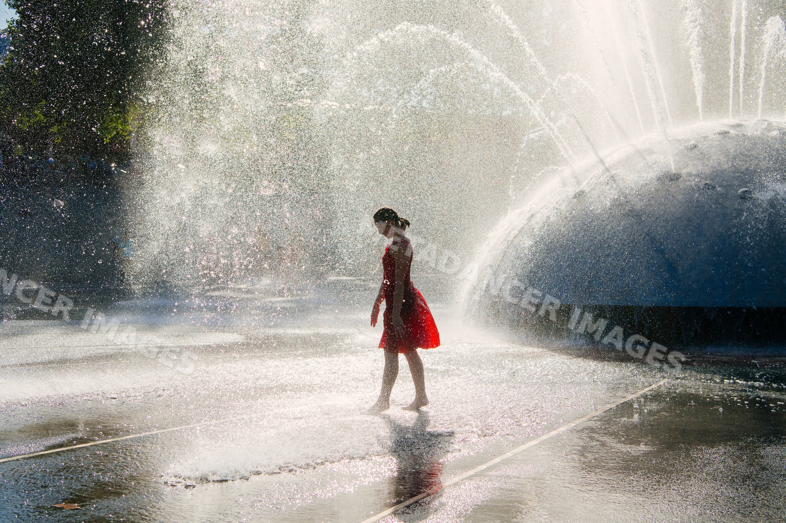 White girl walking barefoot through water fountain spray on sunny day