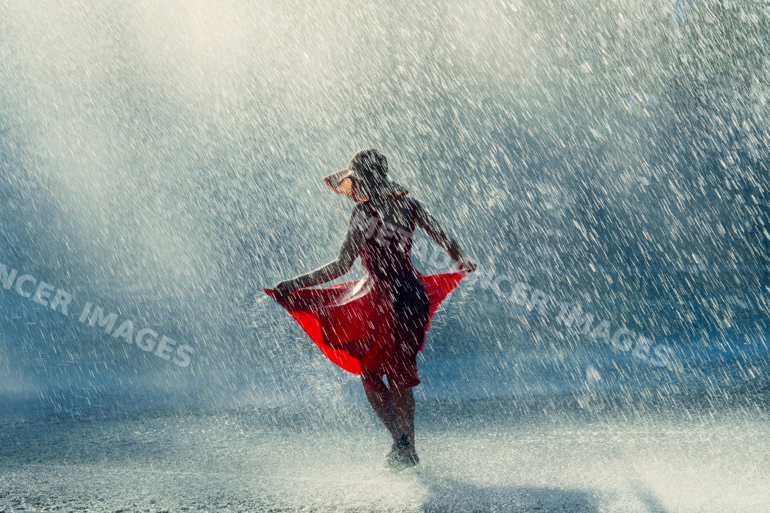 White woman dancing joyfully in rain wearing red dress and sun hat