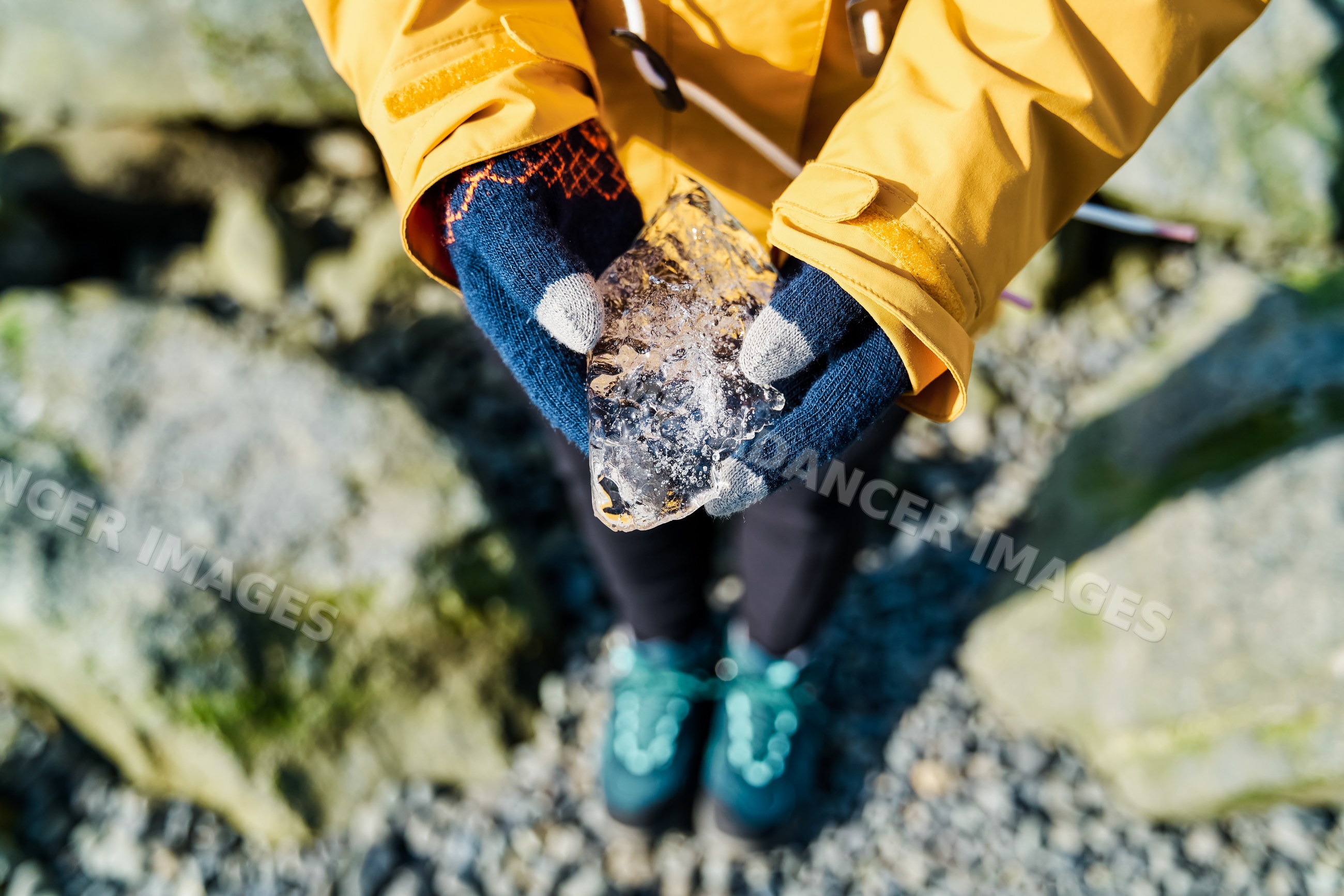 White Person holding a chunk of ice outdoors on rocky ground