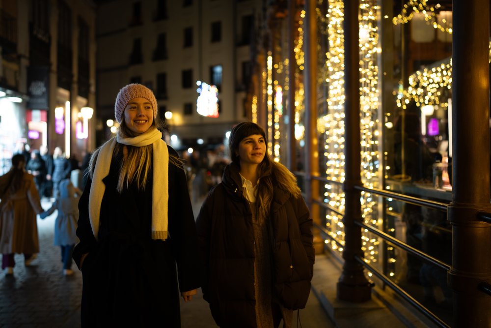 Two white women walking at night with holiday lights in Madrid