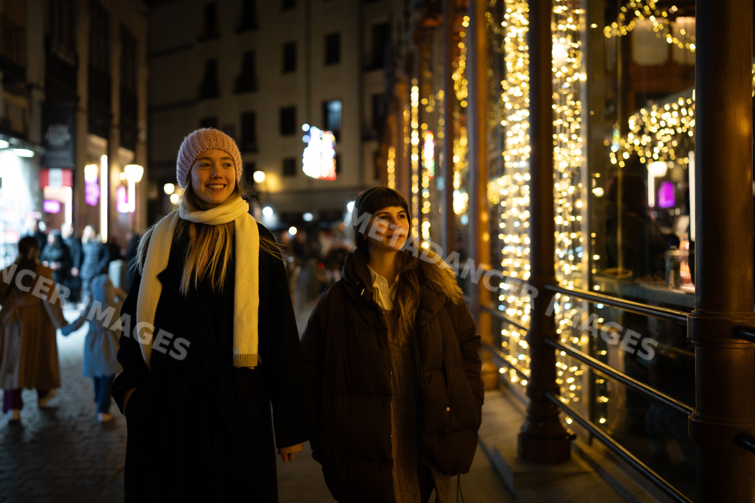 Two white women walking at night with holiday lights in Madrid