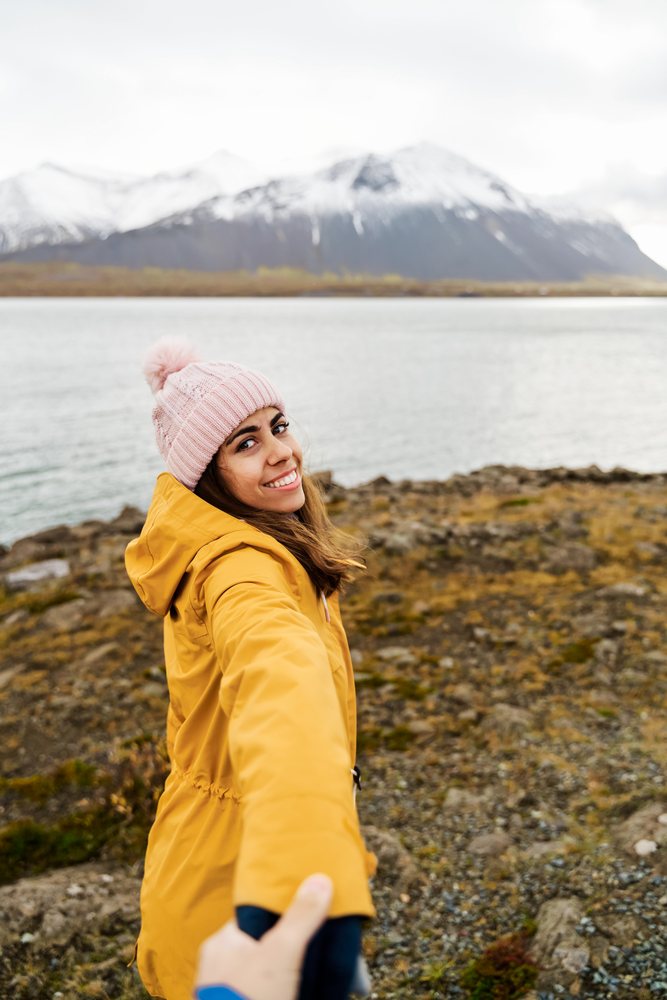 A white woman wearing a yellow jacket holds a hand by a lake