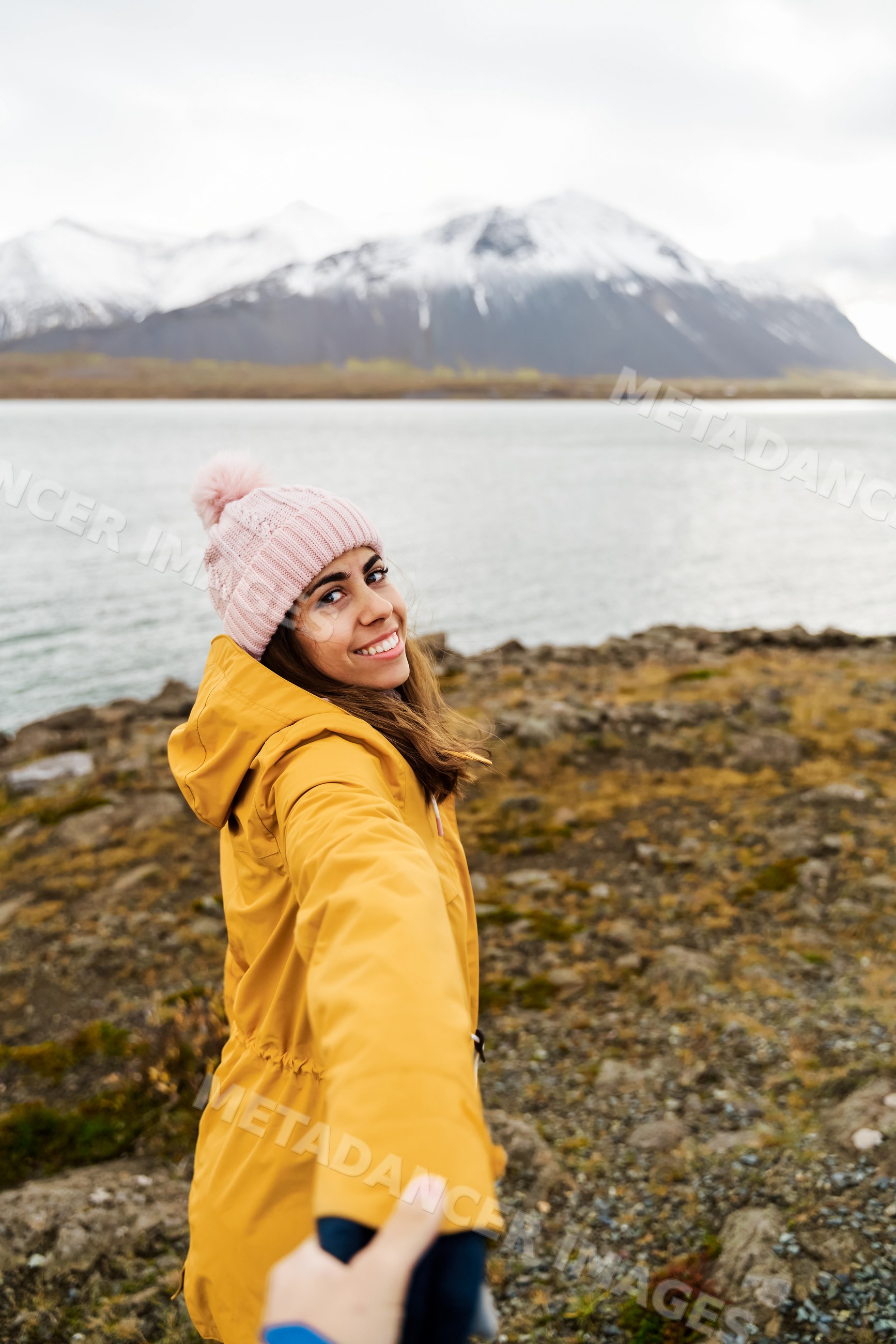 A white woman wearing a yellow jacket holds a hand by a lake